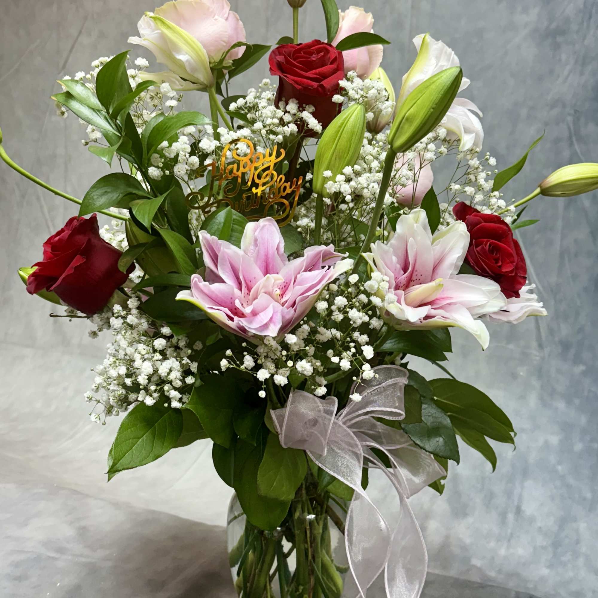 Mixed bouquet of roses and lilies in a glass vase with a birthday pick