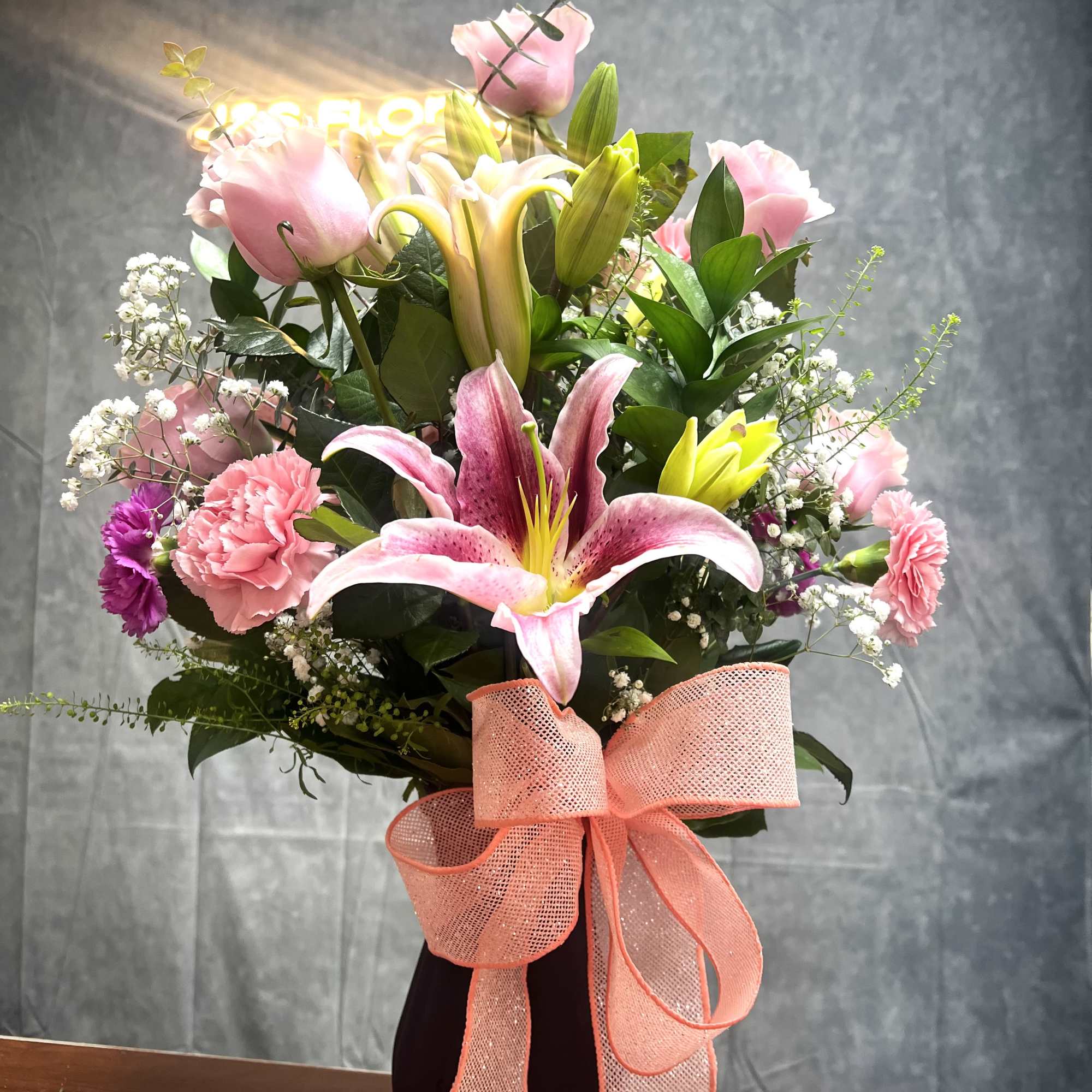 Pink lilies and carnations in a dark vase with a peach ribbon