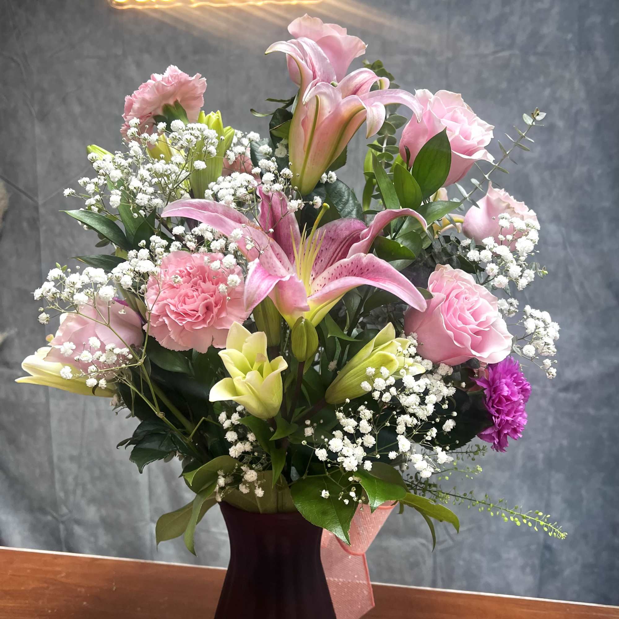 Pink lilies and roses arranged in a dark vase