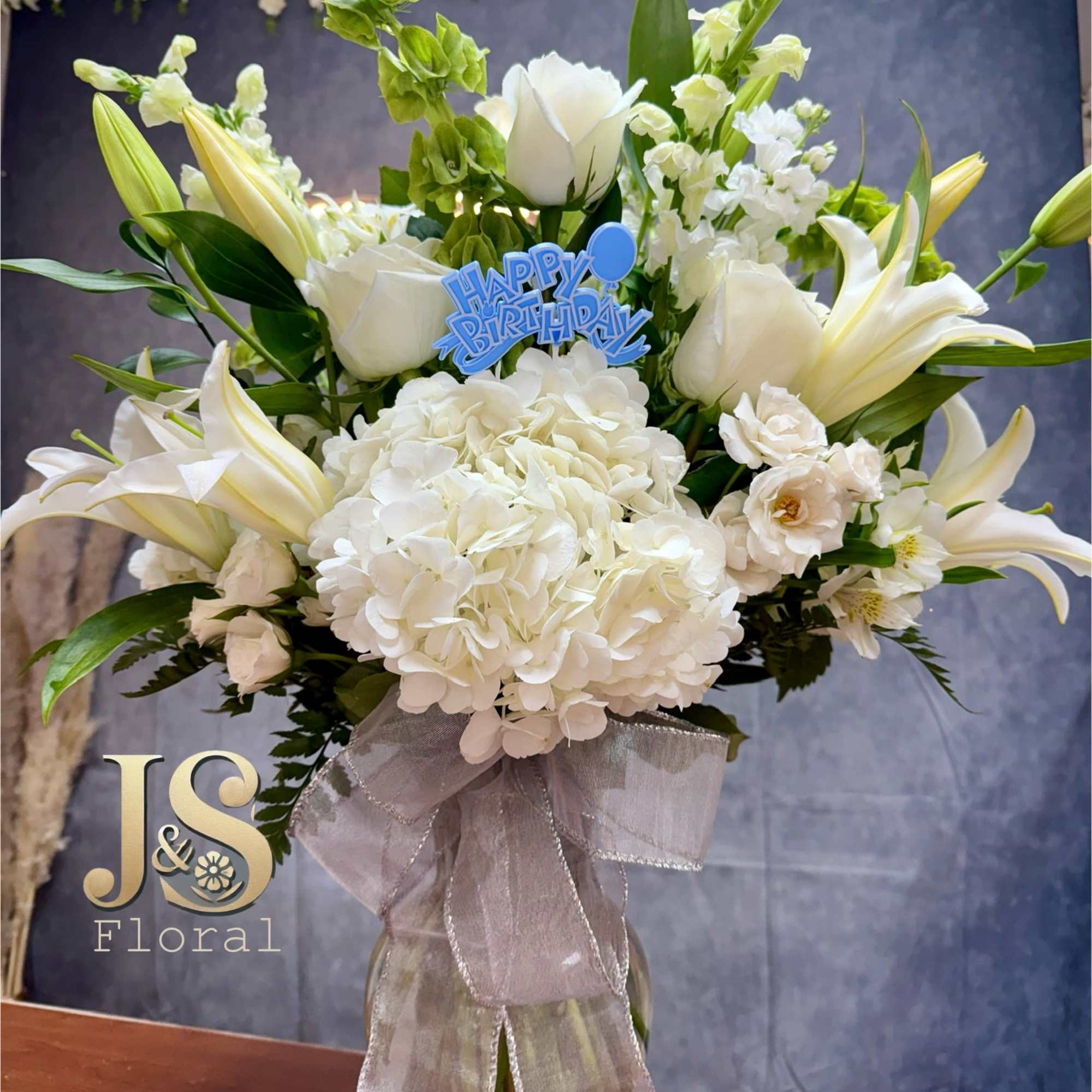 White floral arrangement in a glass vase with a birthday pick