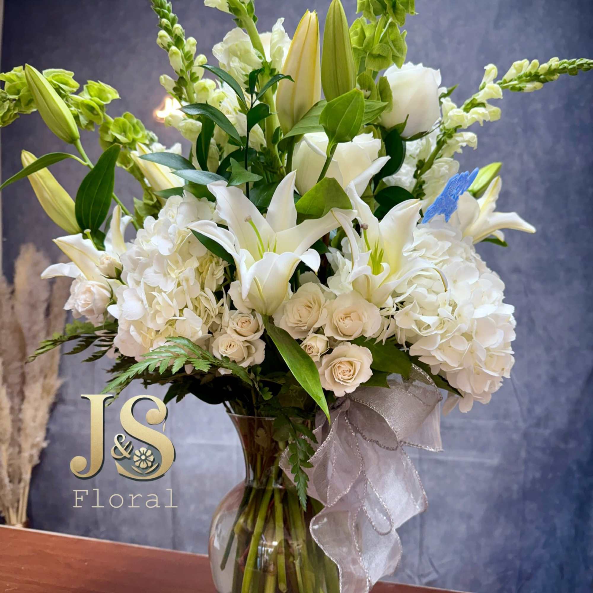 White lilies and roses arranged in a glass vase with a sheer ribbon.