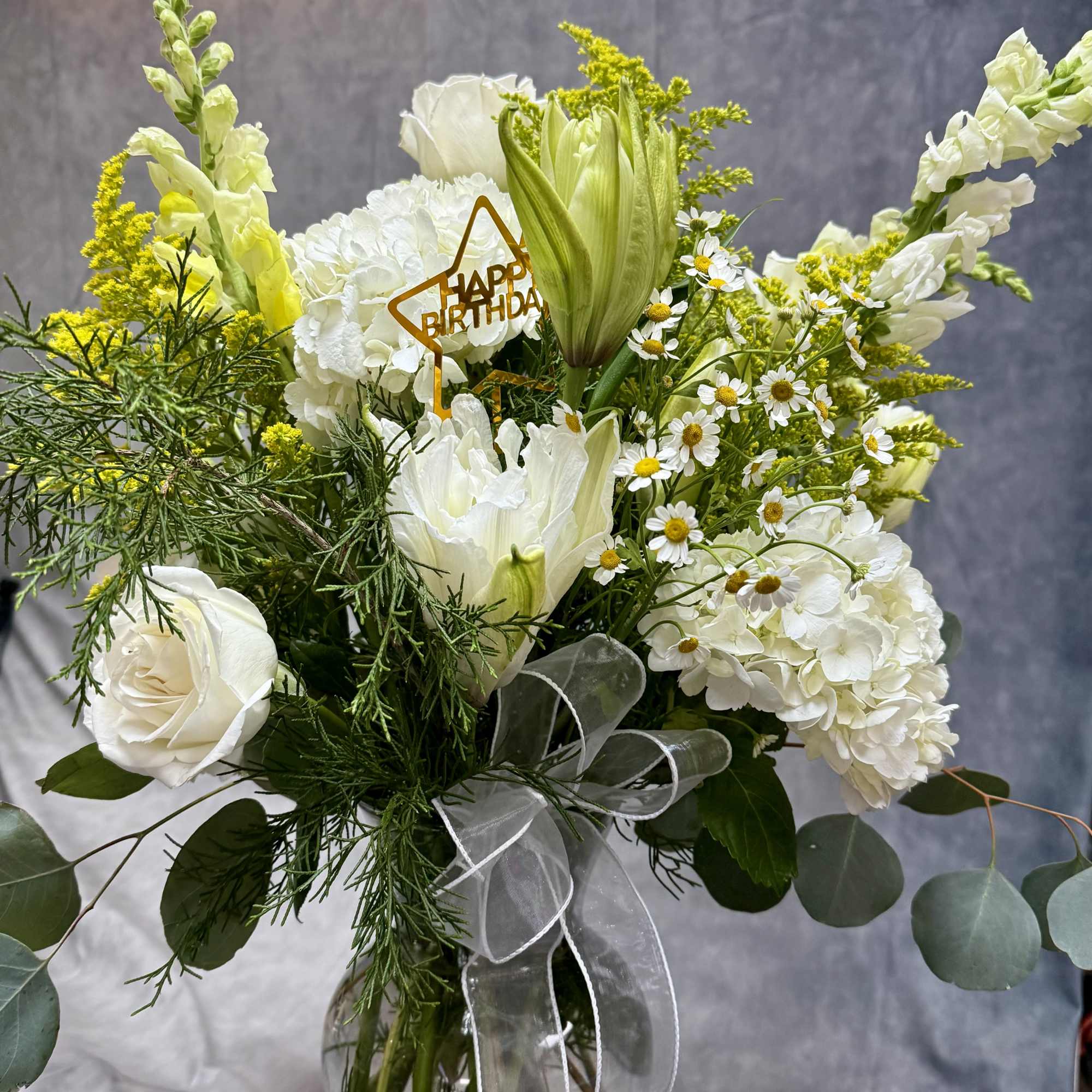 White floral bouquet in a glass vase with a birthday pick