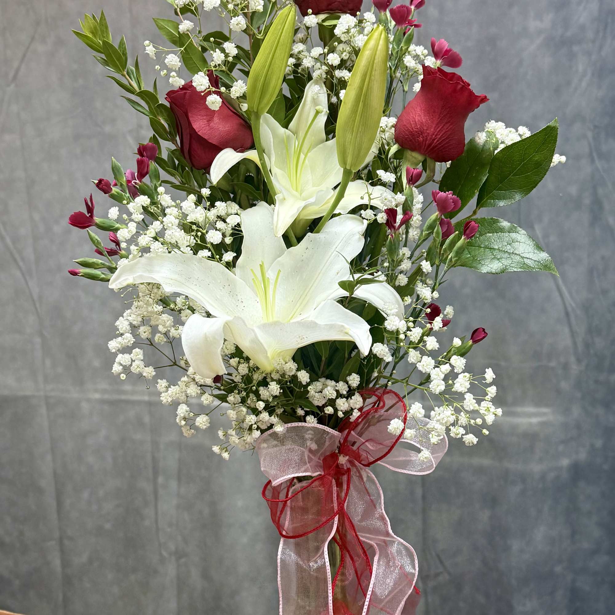 Tall bouquet of white lilies and red roses in a glass vase