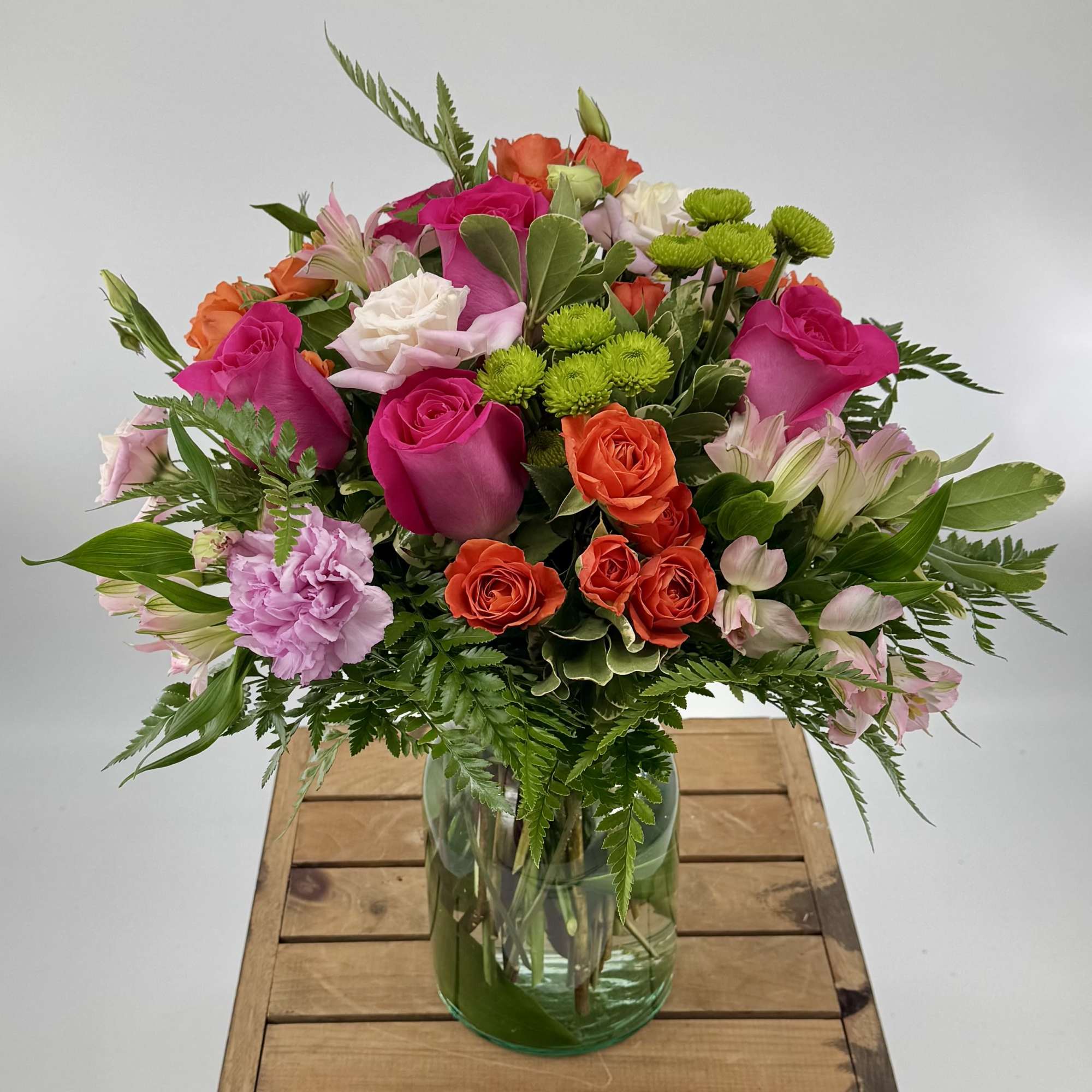 Mixed bouquet of pink, orange, white, and green flowers in a glass vase