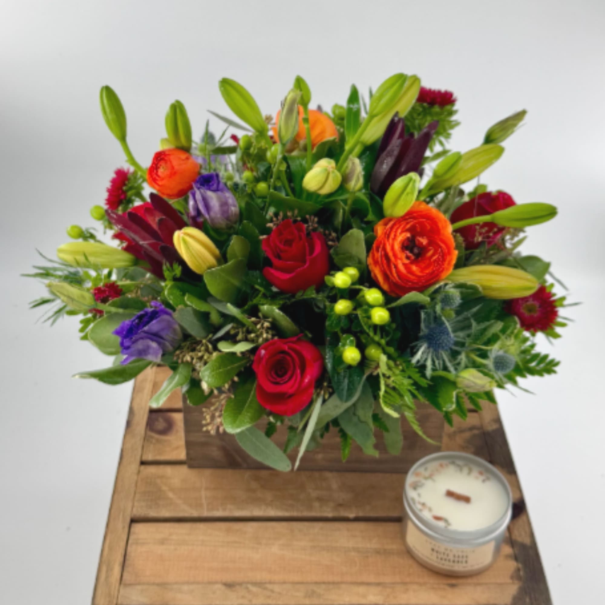 Colorful mixed flower arrangement in a wooden box with a candle beside it