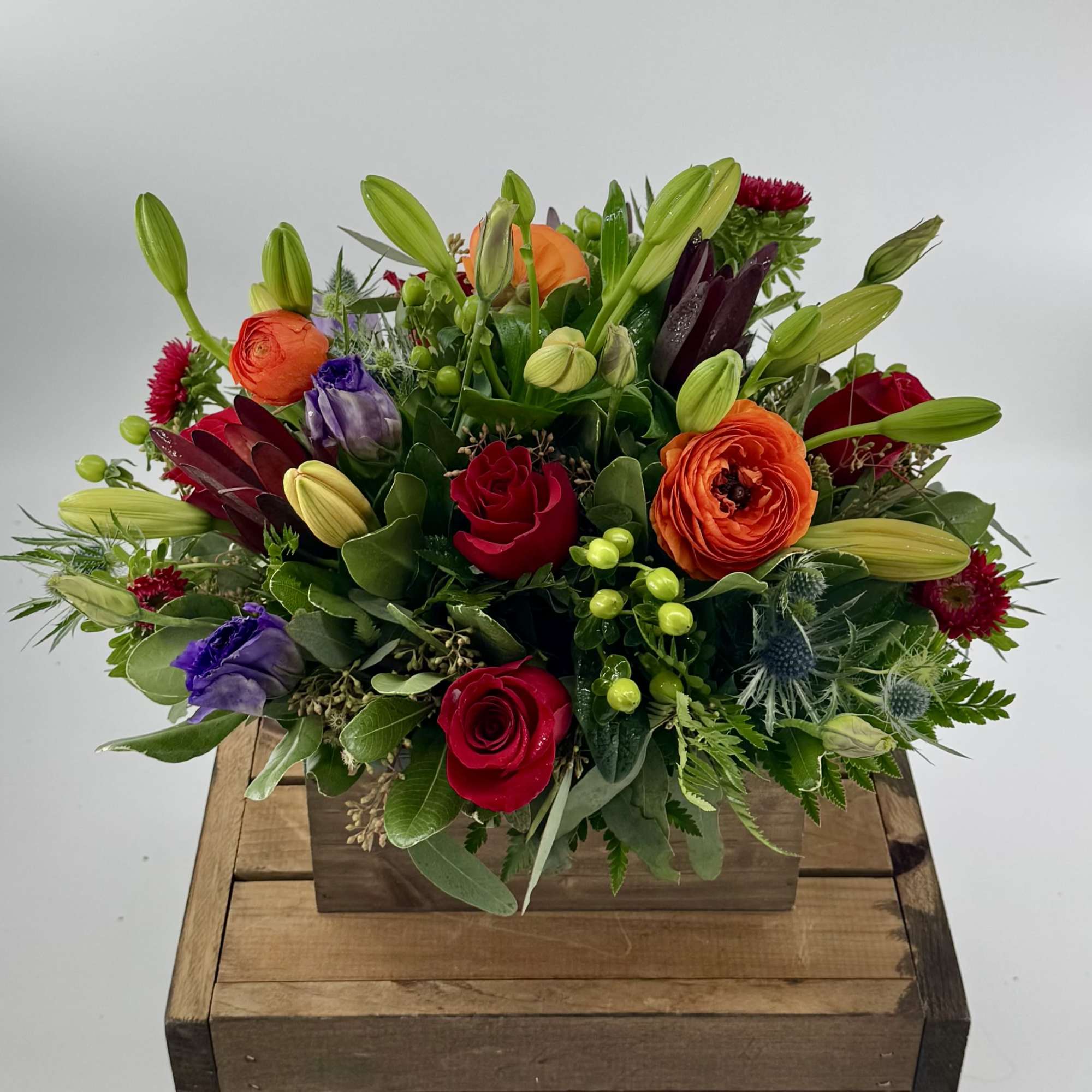 Mixed bouquet of roses, lilies, and ranunculus in a wooden box