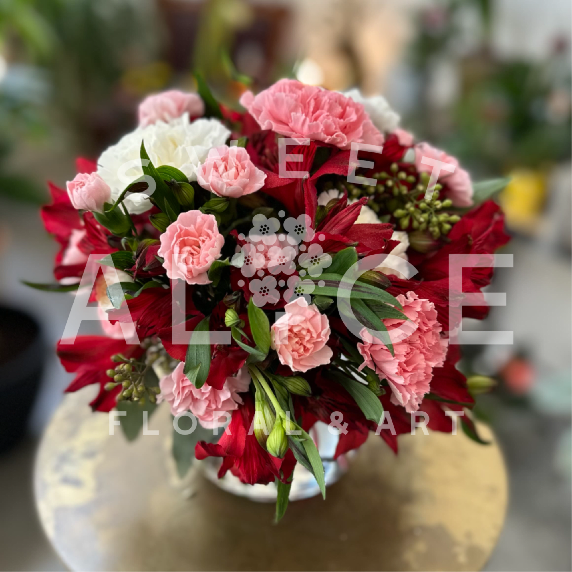 Round arrangement of pink and white carnations with deep red lilies in a white vase