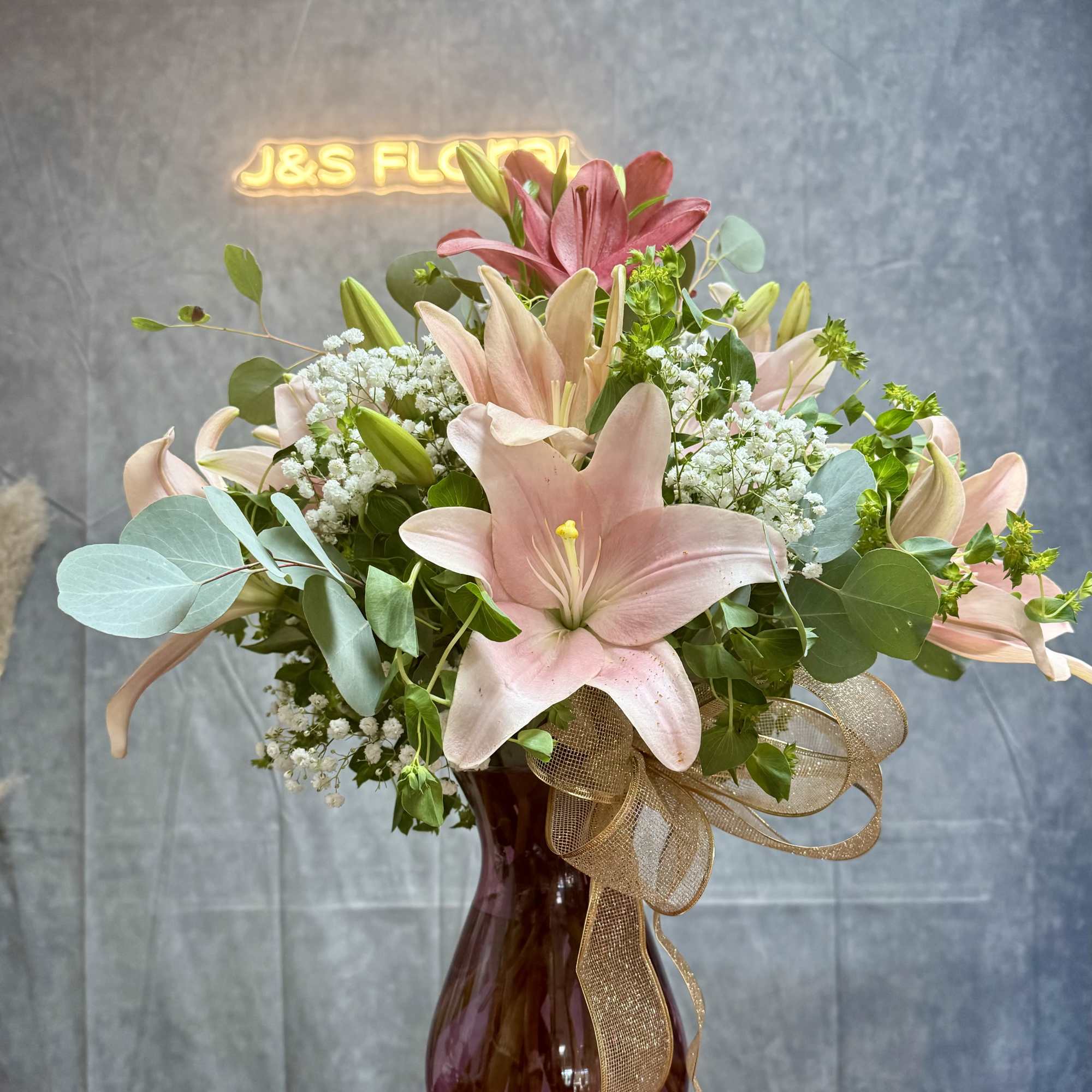 Pink lilies in a burgundy vase with a gold ribbon bow