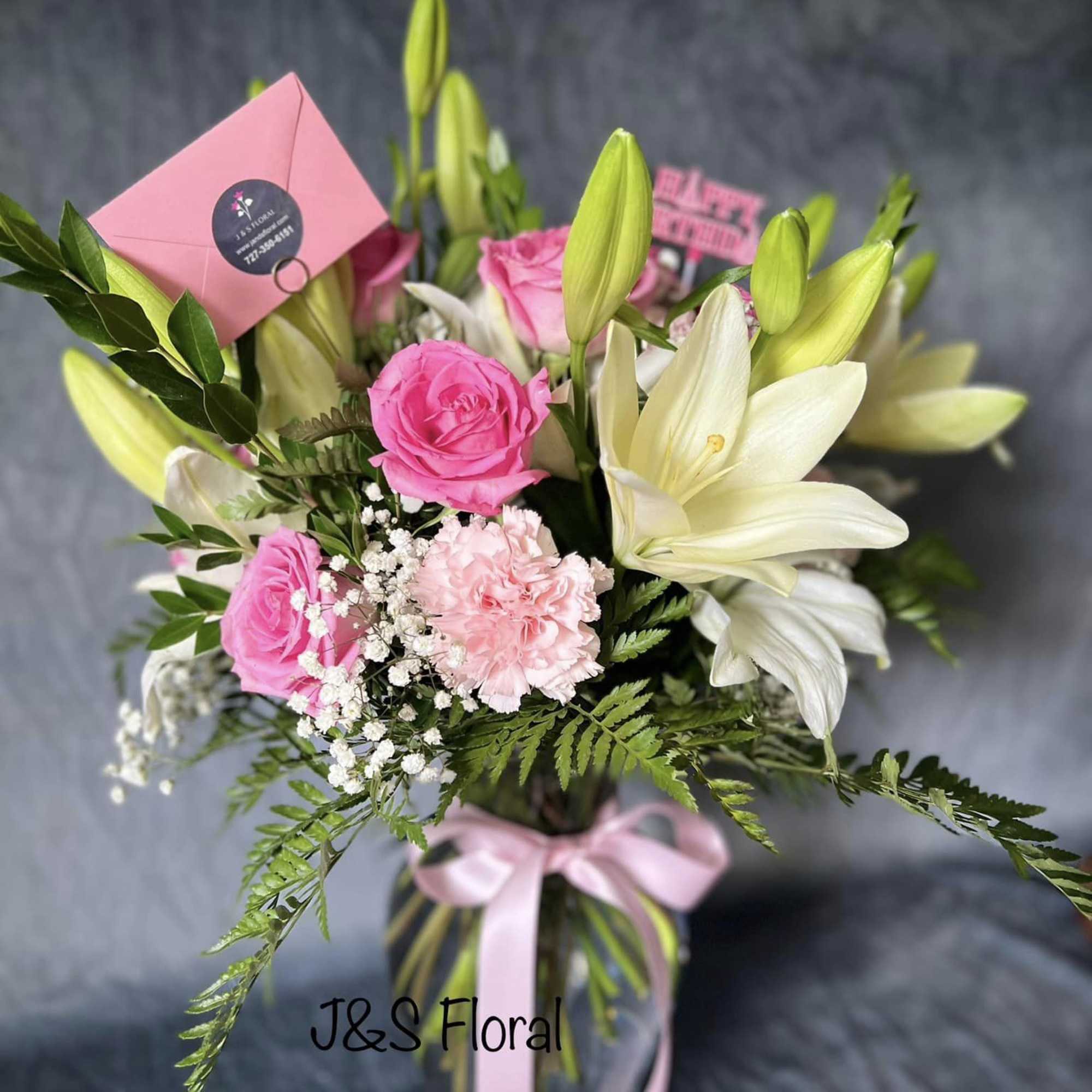 Pink roses and white lilies in a glass vase with a pink ribbon