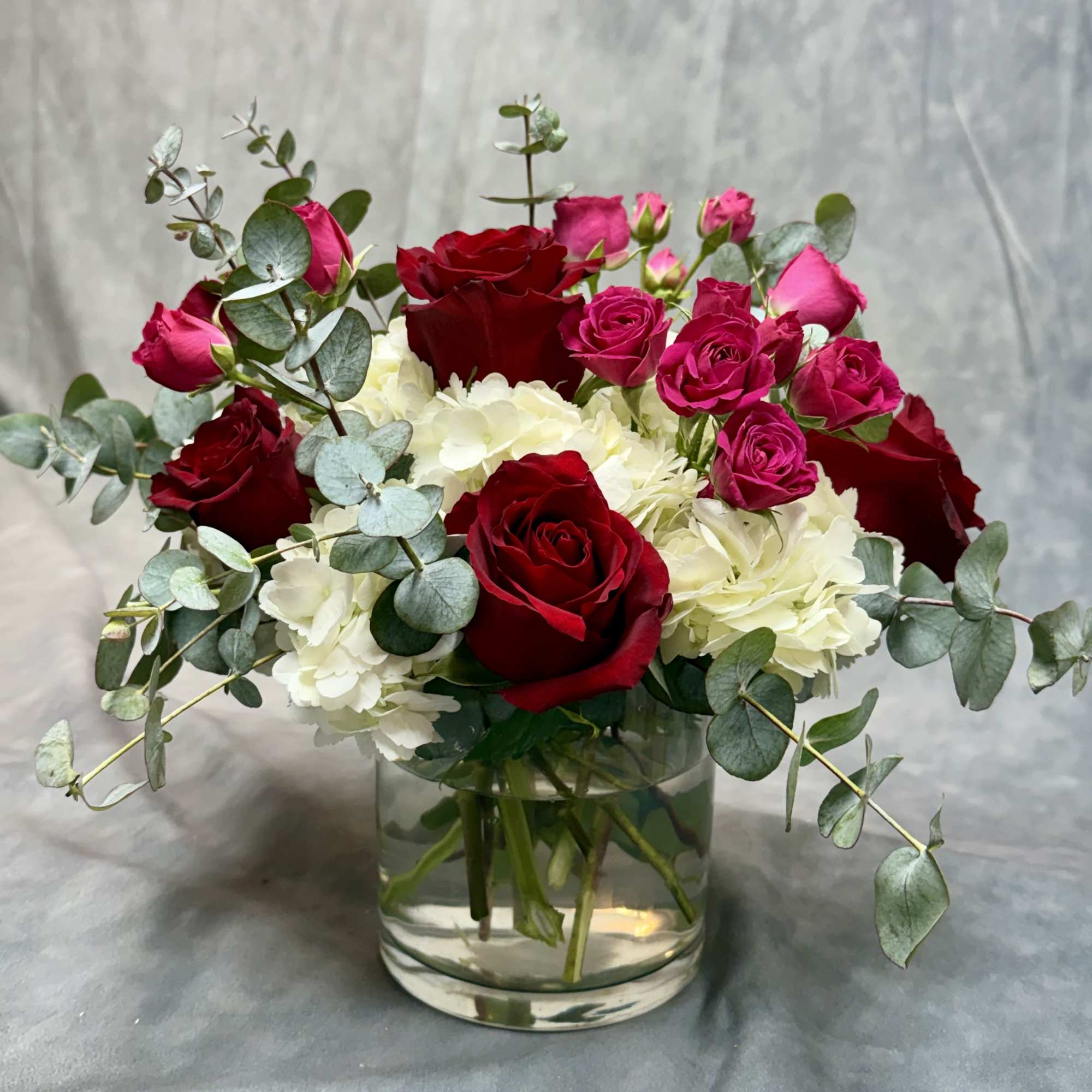 Red and pink roses with white hydrangeas in a glass vase