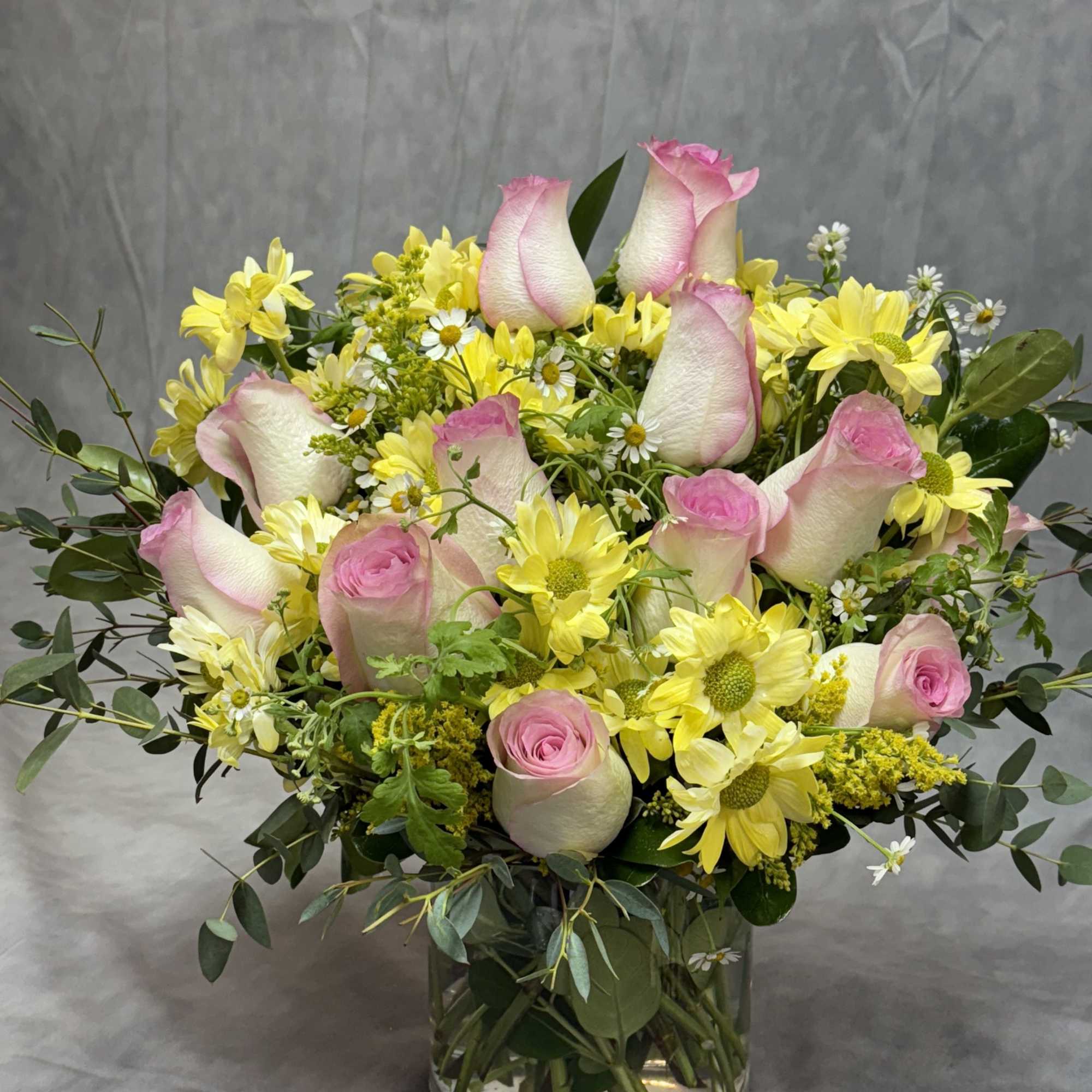 Pink roses and yellow daisies arranged in a clear glass vase