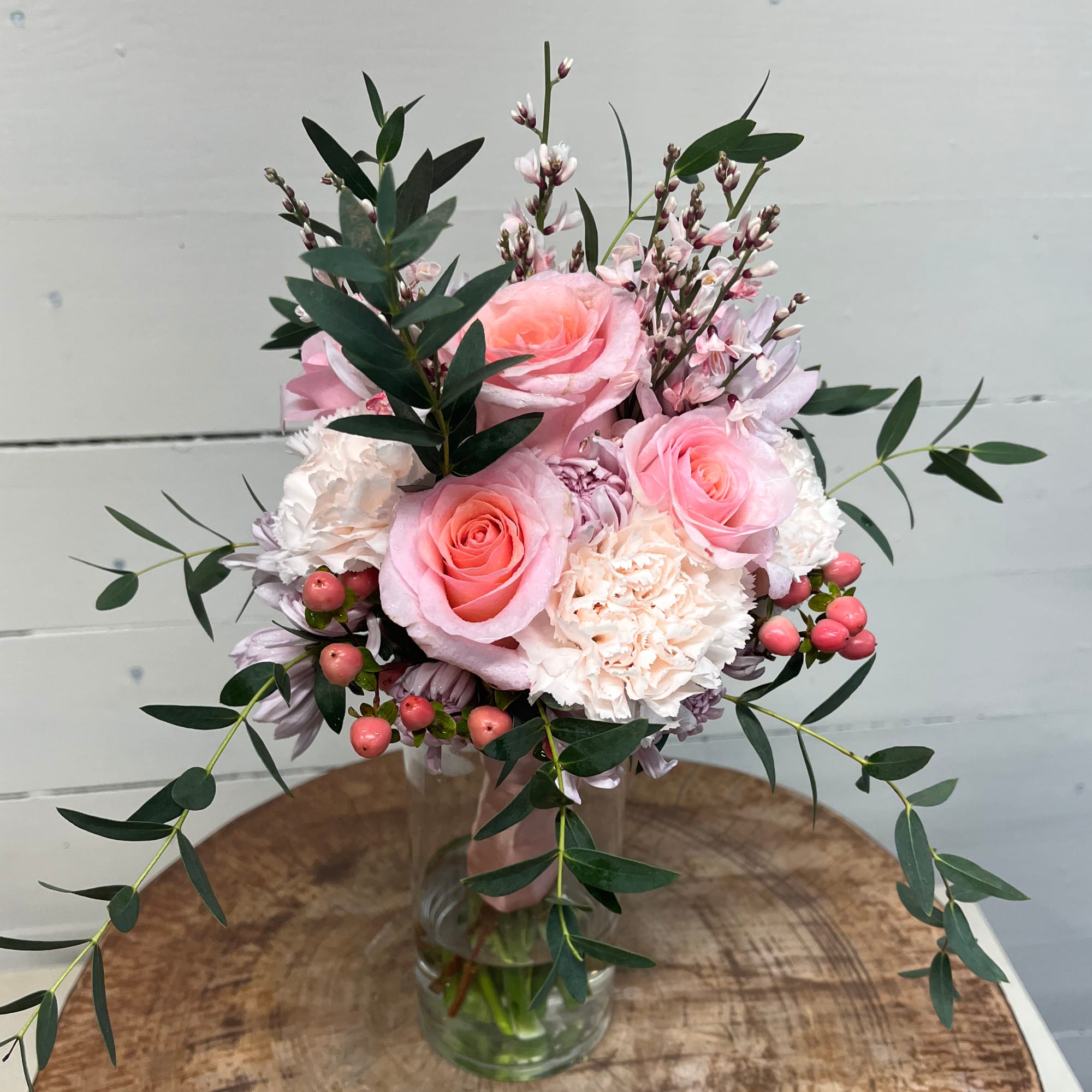 Pink roses and carnations in a glass vase with trailing greenery
