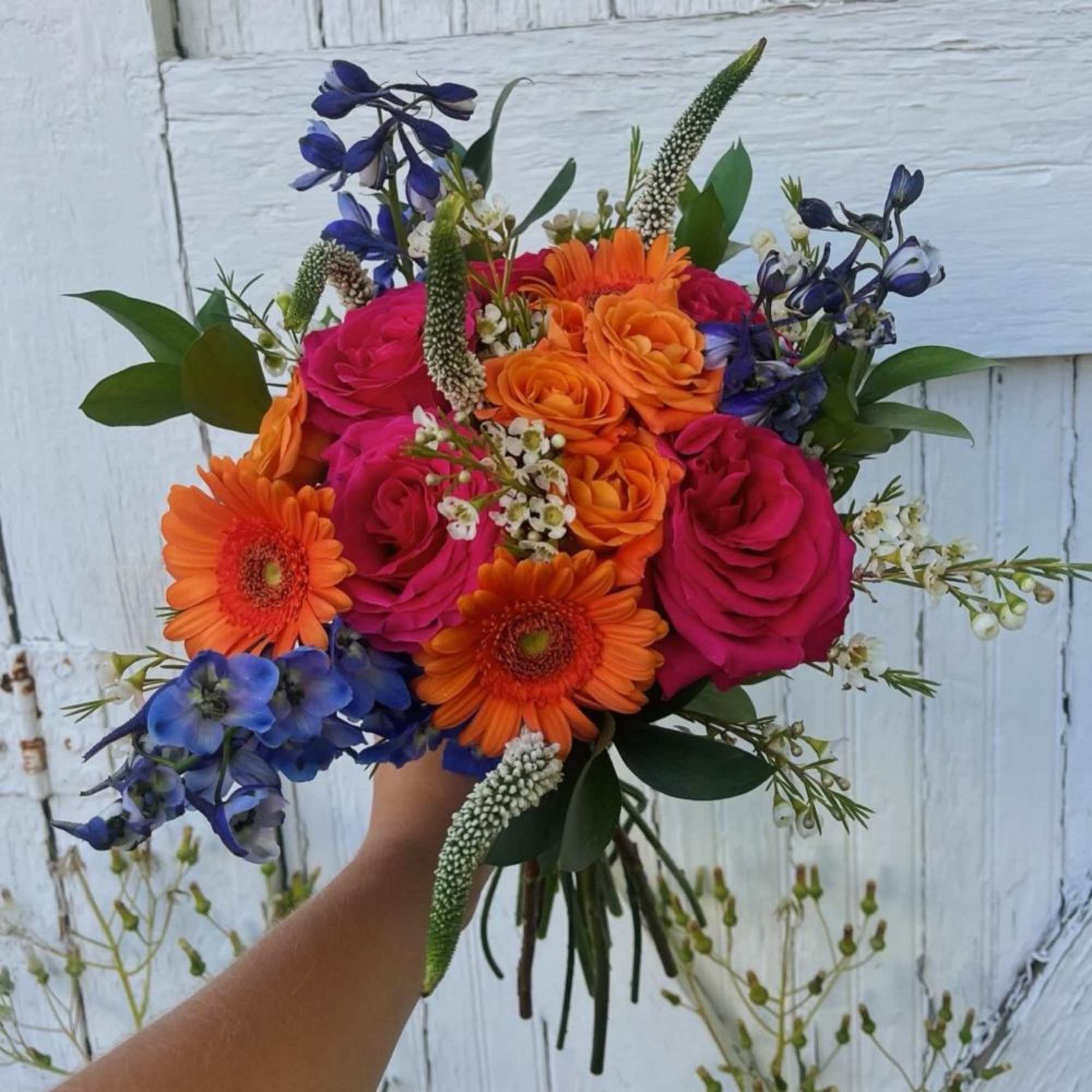 Handheld bouquet of orange and pink roses with blue flowers