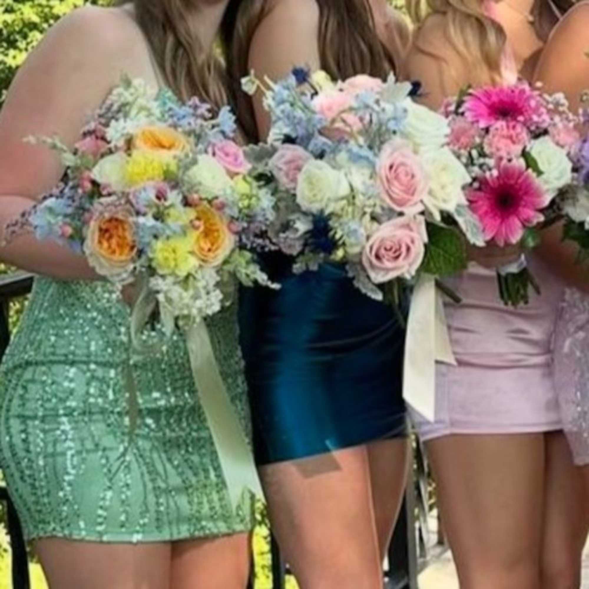 Three women hold pastel mixed flower bouquets at an outdoor event.