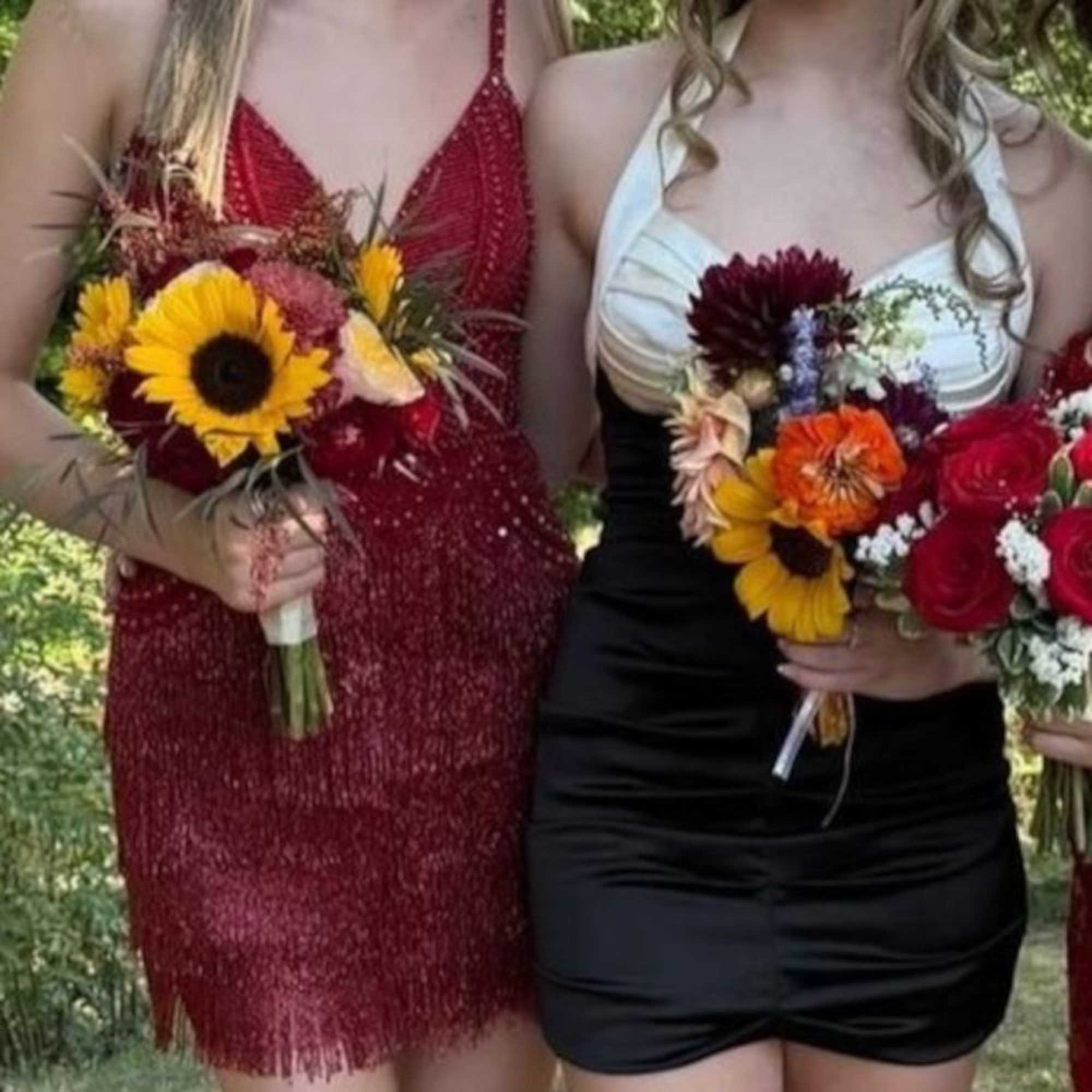 Two women hold colorful bouquets with sunflowers and roses