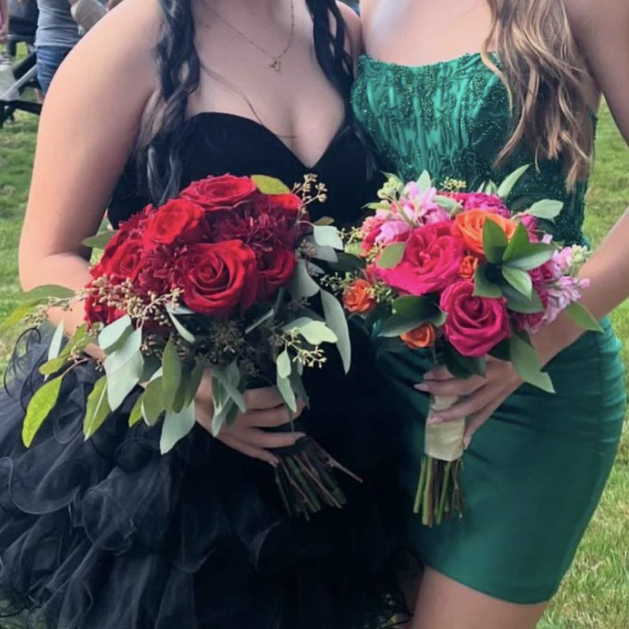 Two women hold bouquets of red and pink roses with greenery.