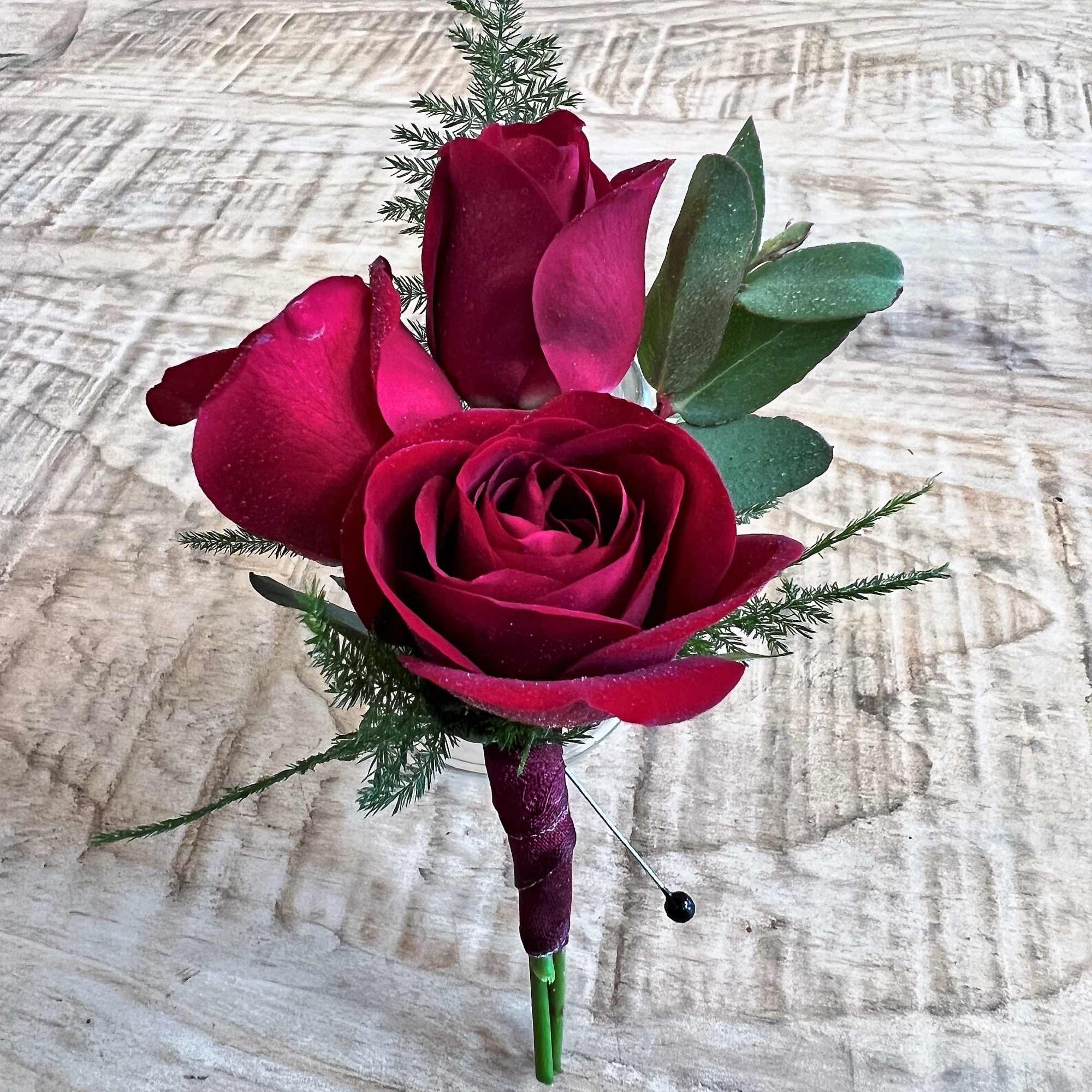 Deep red rose boutonniere with greenery on a wrapped stem