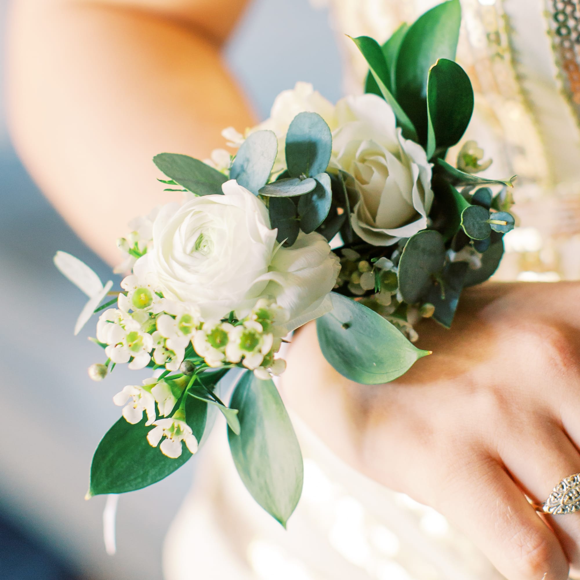 White floral wrist corsage with green foliage on a person's hand