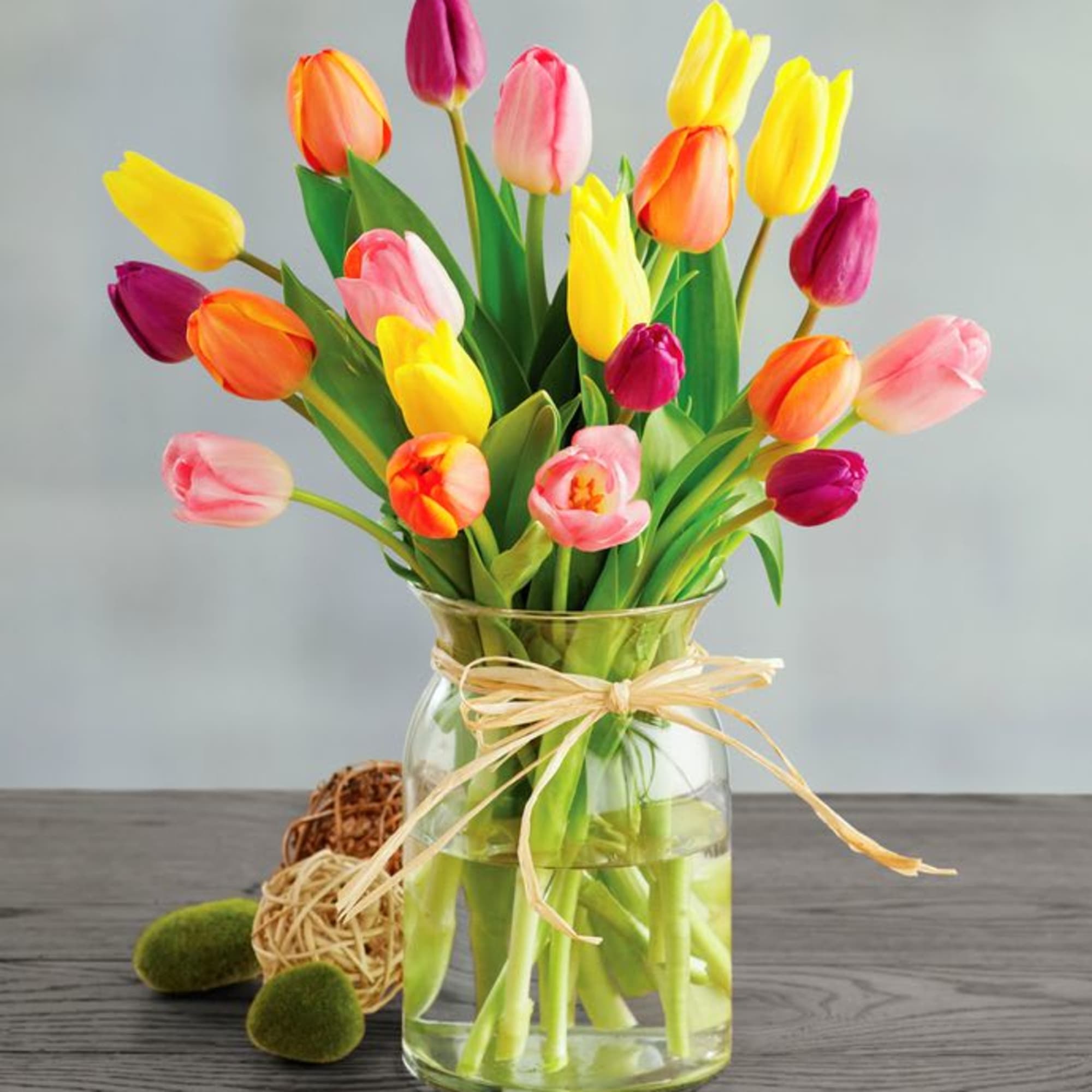 Colorful tulips arranged in a clear glass vase with a ribbon bow.