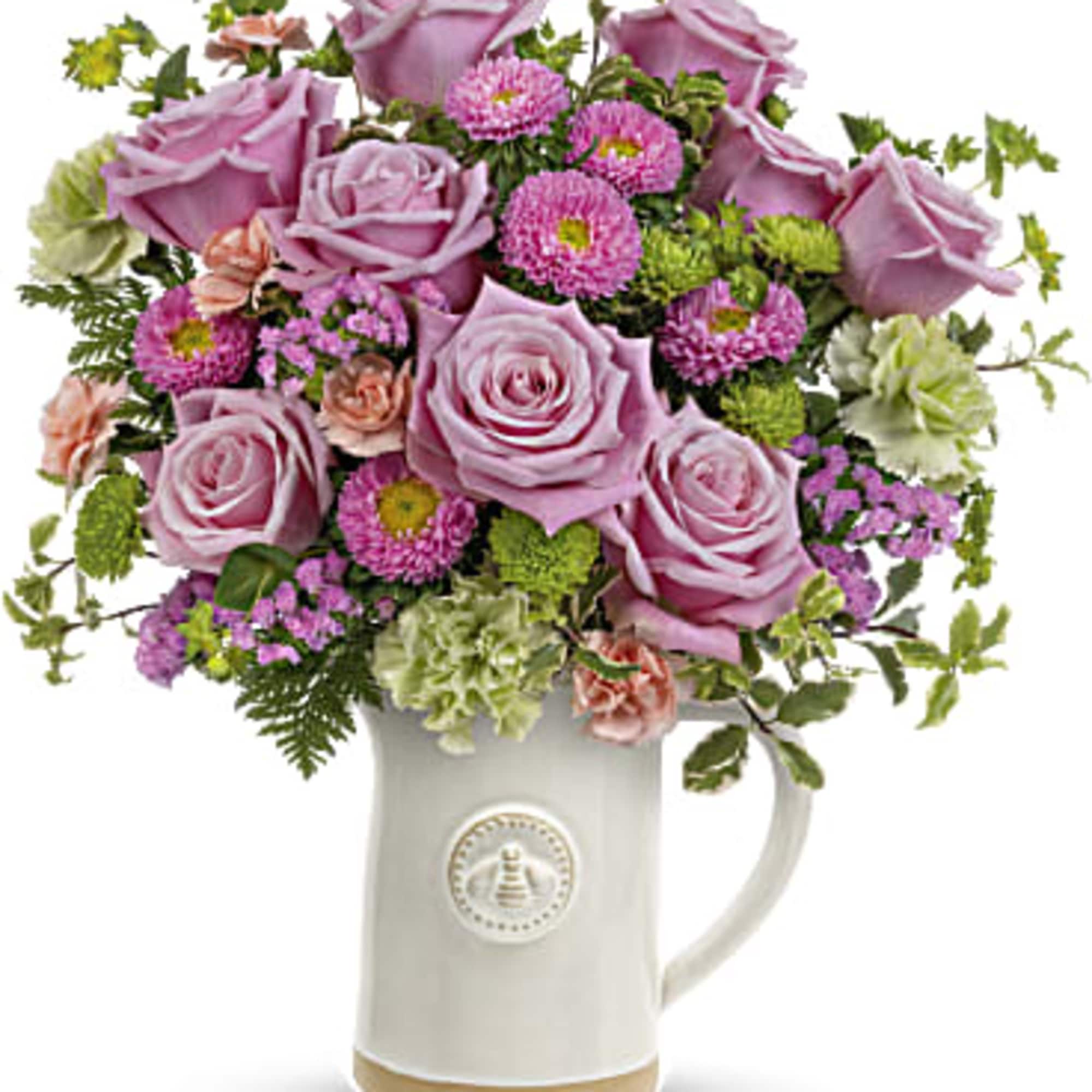 Pink roses and mixed blooms arranged in a white ceramic pitcher