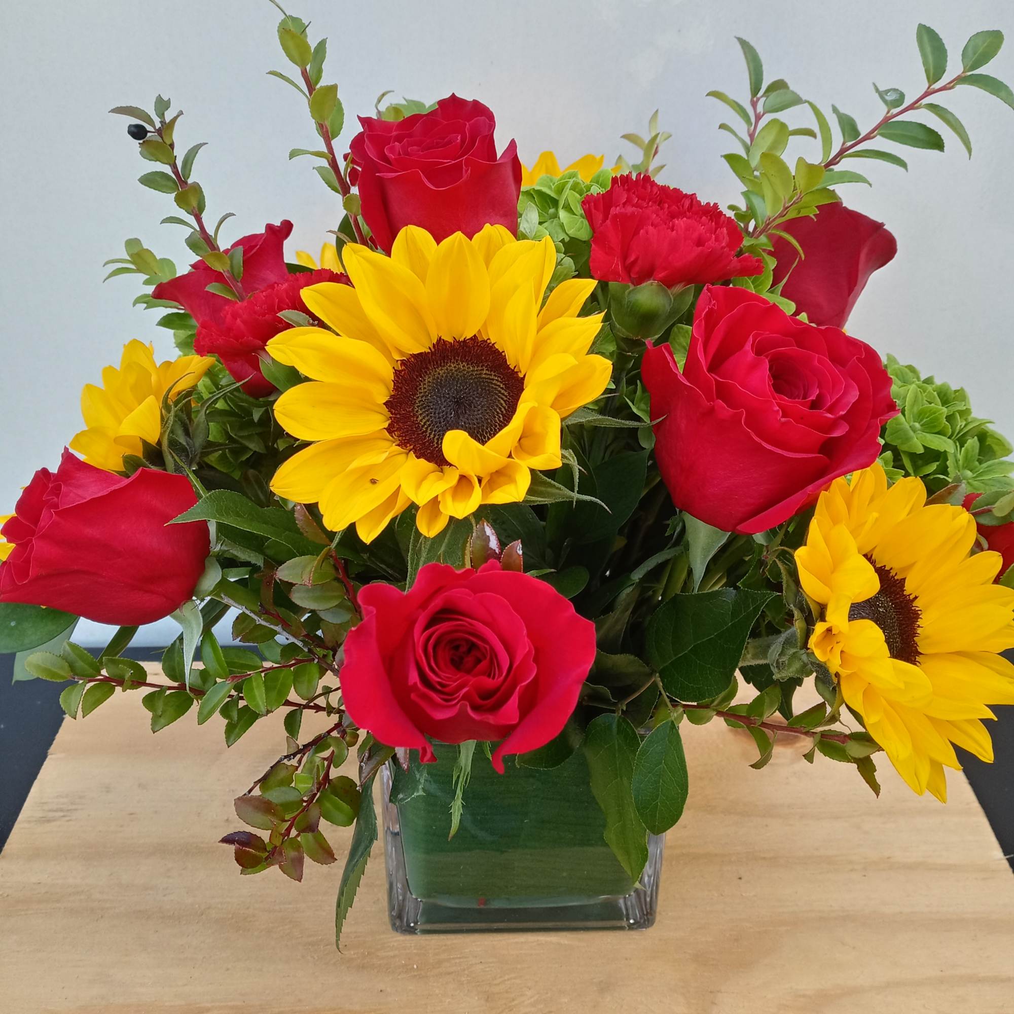 Red roses and yellow sunflowers in a square glass vase