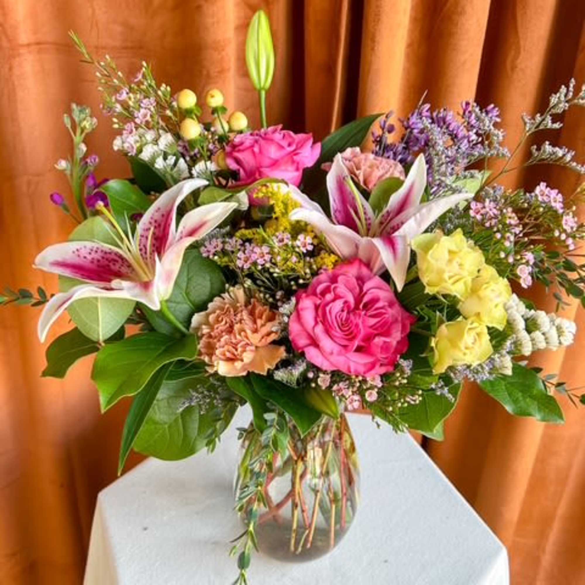 Mixed bouquet of pink roses, lilies, and yellow blooms in a glass vase