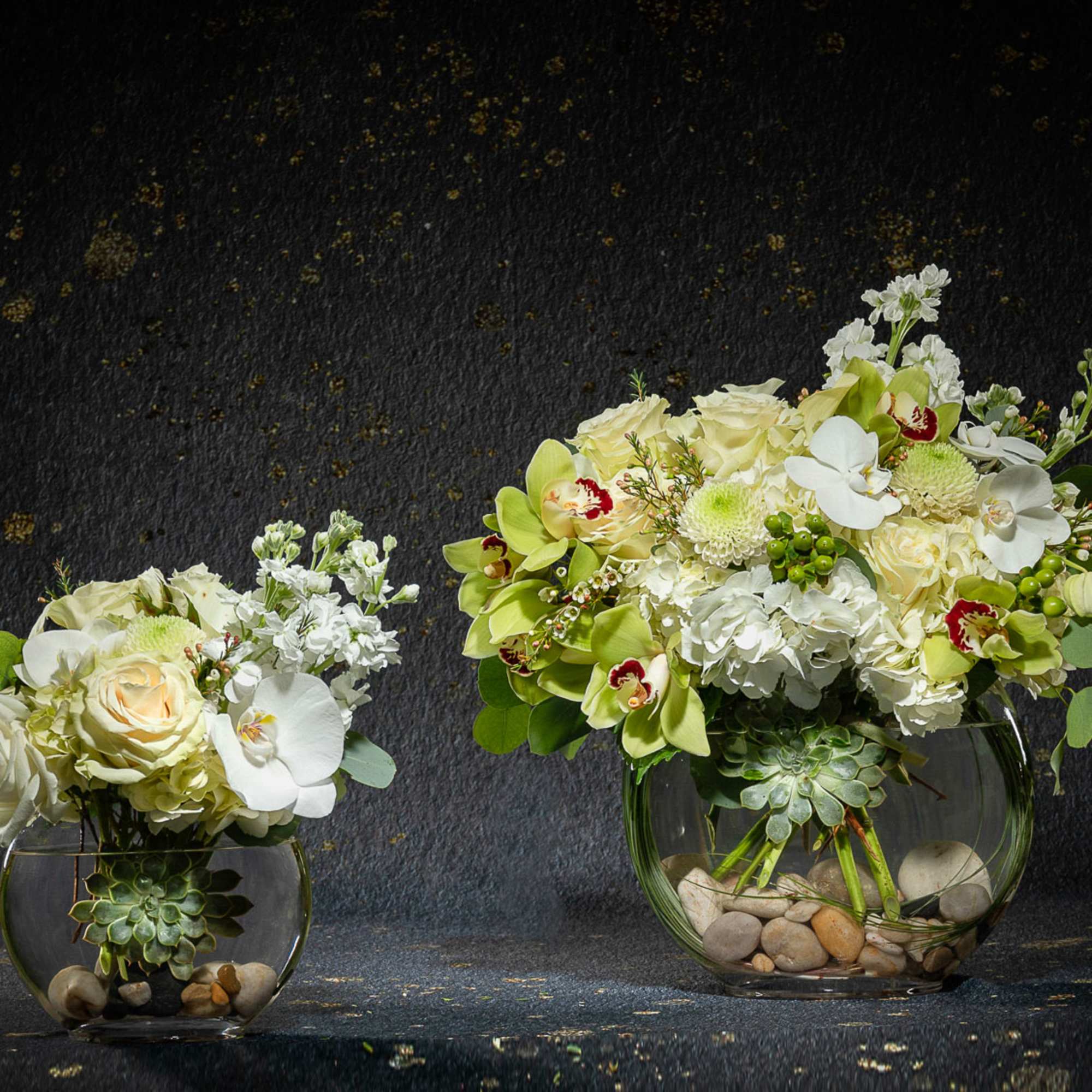 Two white floral arrangements in glass bowls with succulents and stones