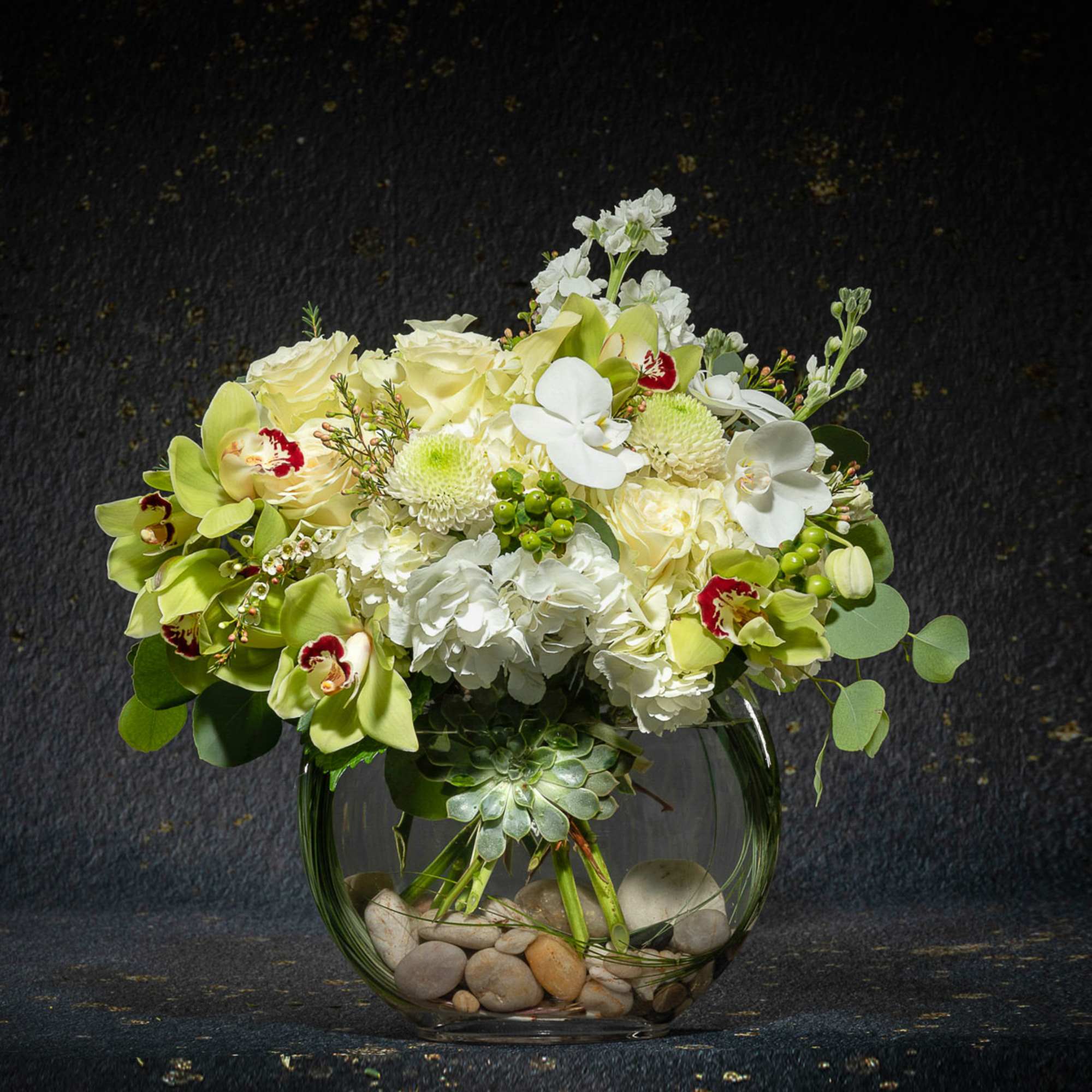 White and pale green floral arrangement in a round glass vase with stones