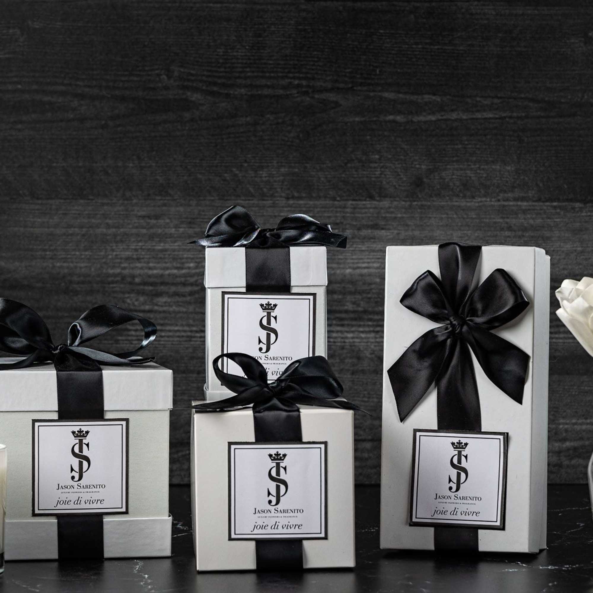 White gift boxes with black ribbons beside a candle and white flowers in vases.