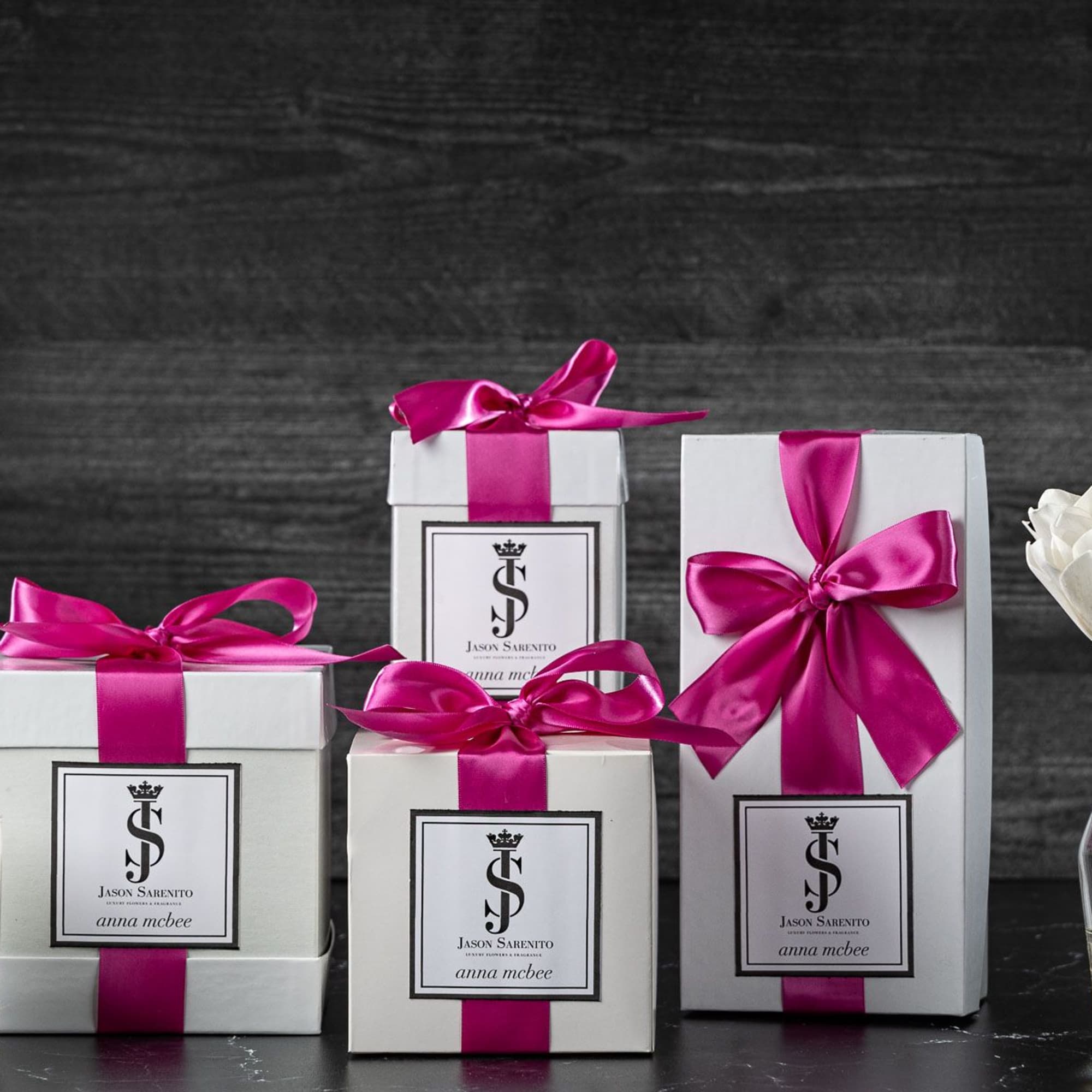 White gift boxes with pink ribbons beside a candle and white flowers in a vase