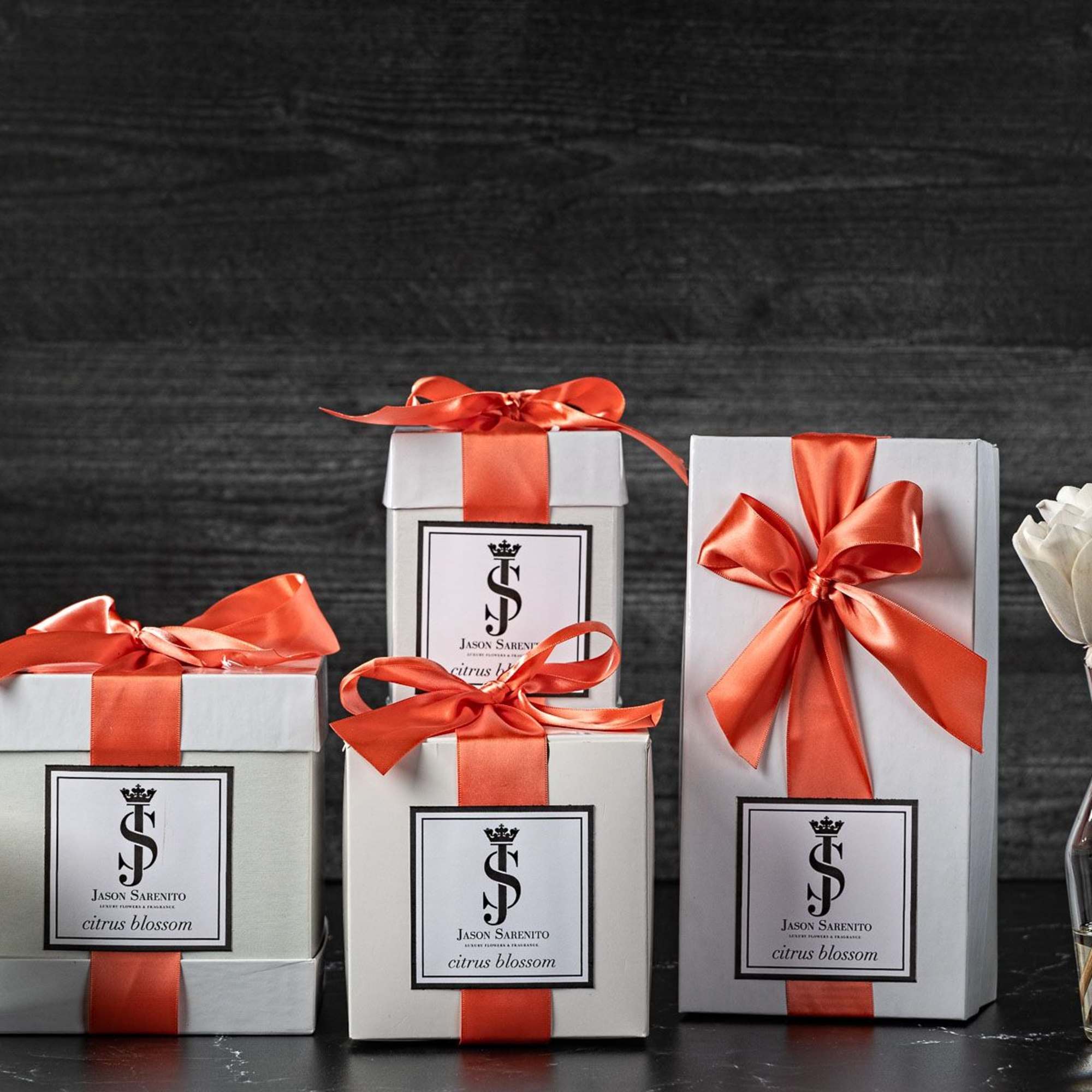 Gift boxes with orange ribbons beside a candle and a small vase of white flowers
