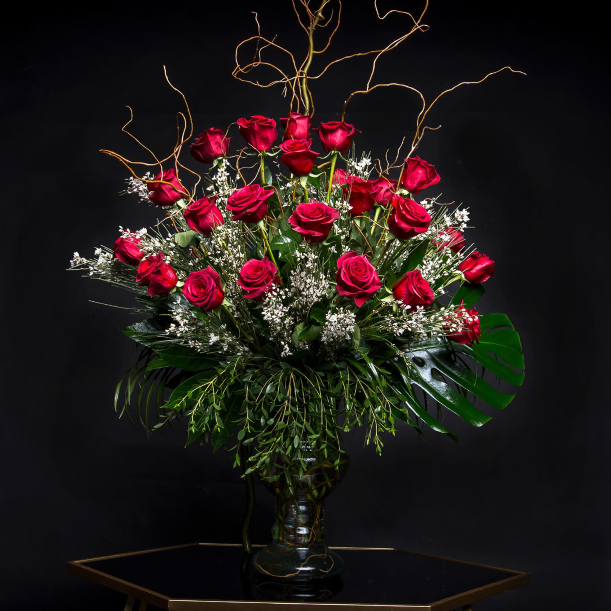 Red roses arranged in a clear glass vase with curly branches