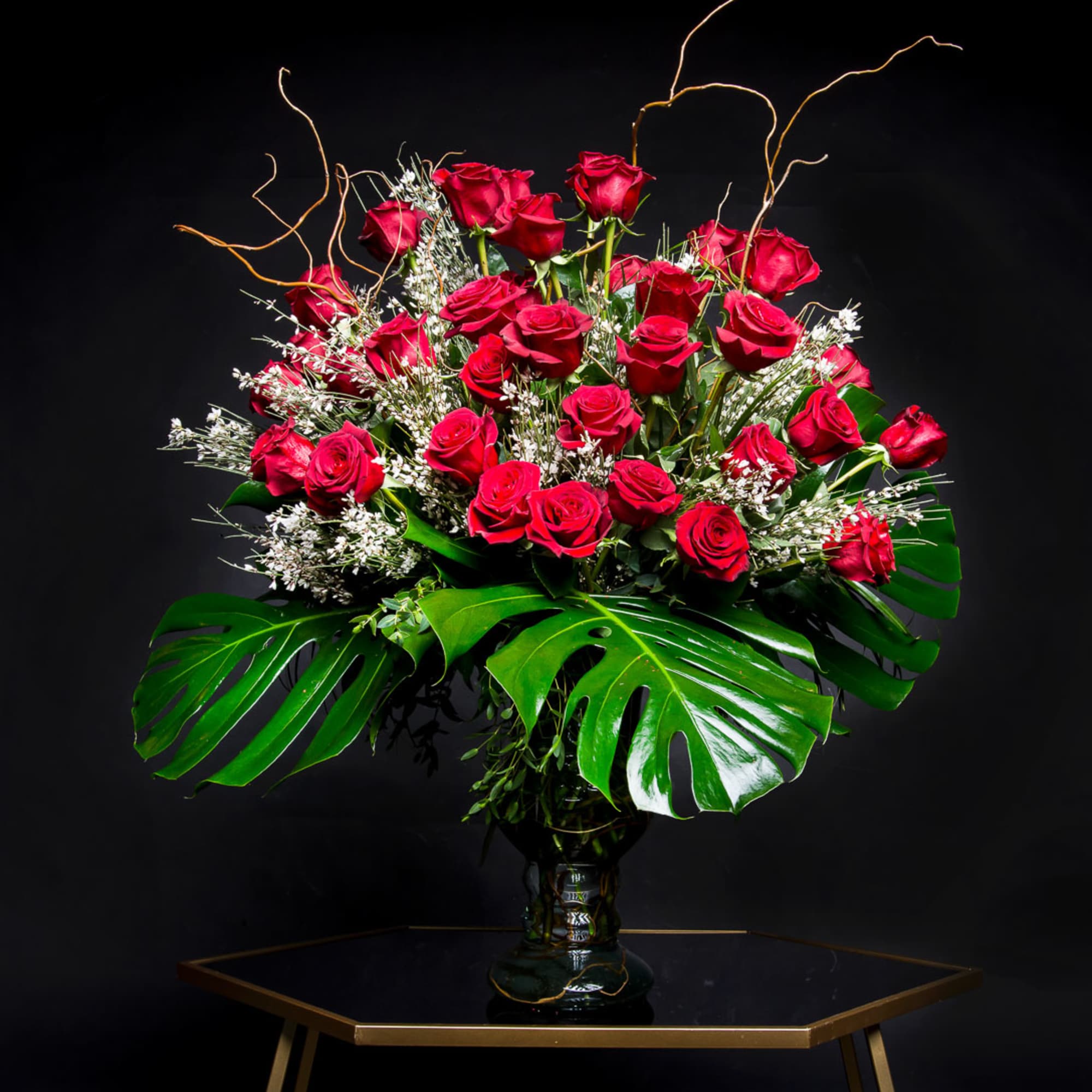 Red roses arranged in a glass vase with large tropical leaves