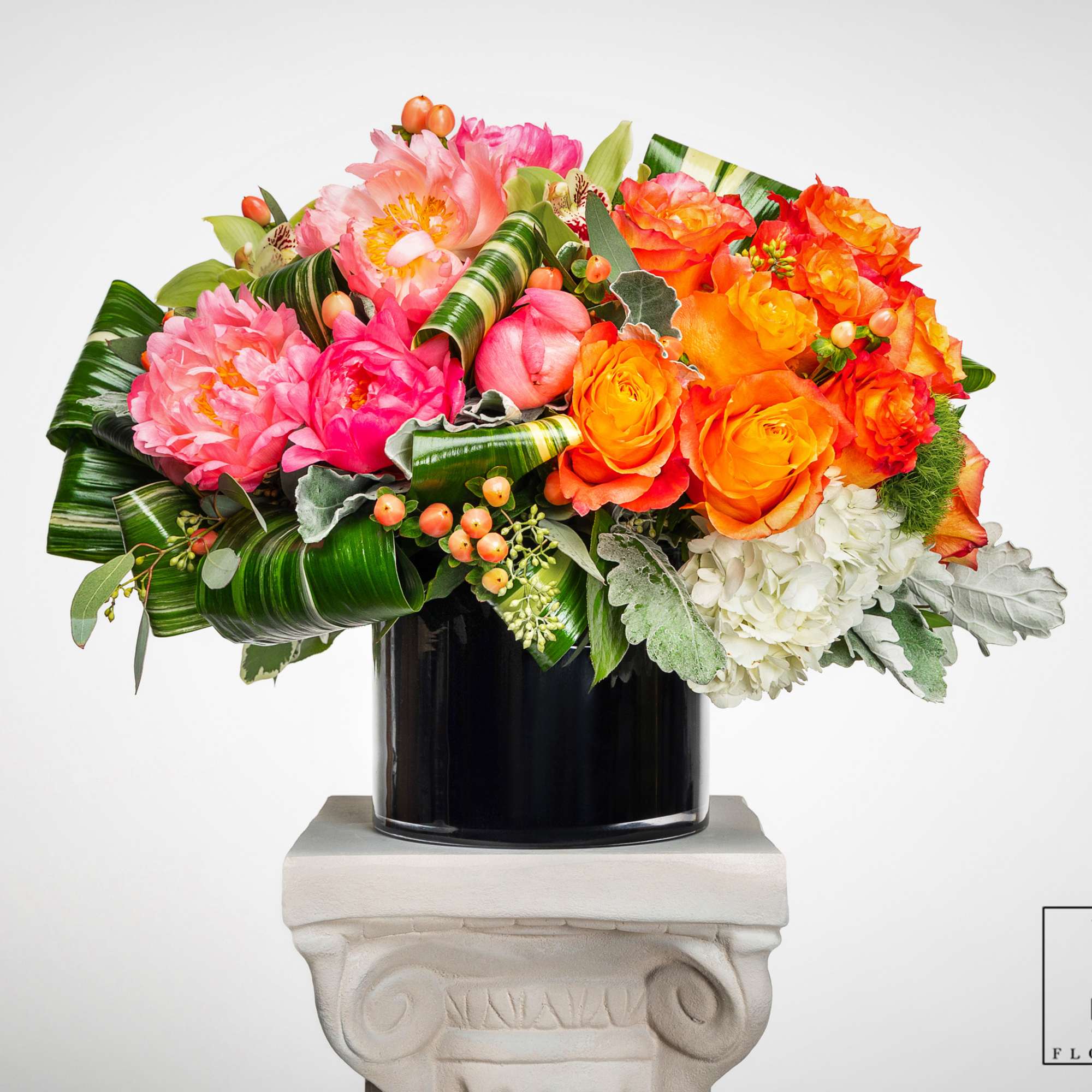 Bright pink peonies, orange roses, and white hydrangeas in a black cylinder vase