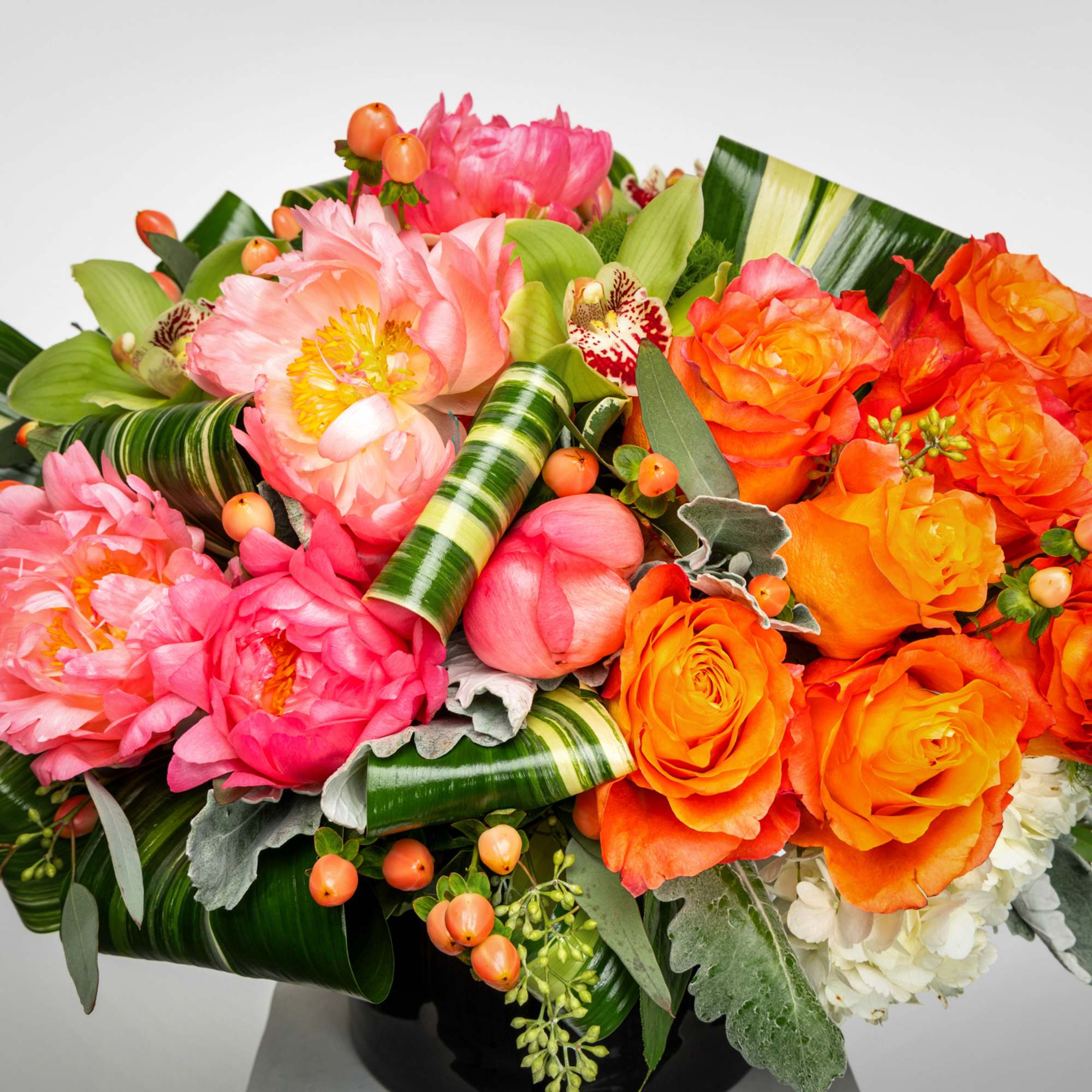 Bright arrangement of pink peonies and orange roses with folded green leaves in a low black vase