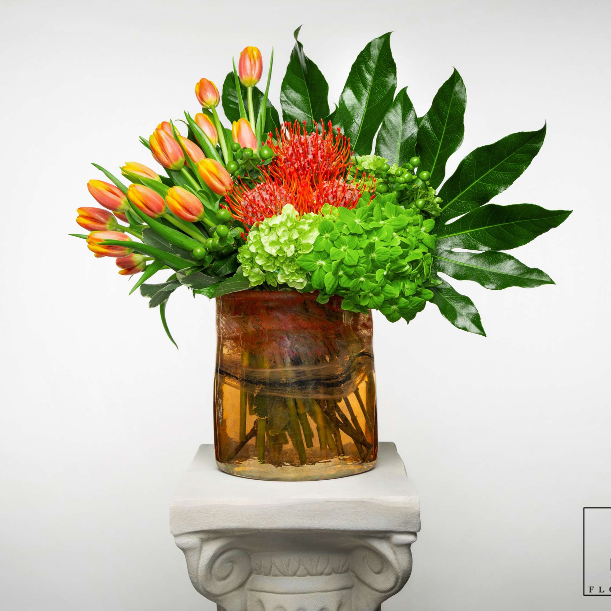 Orange tulips and red tropical flowers in an amber glass vase
