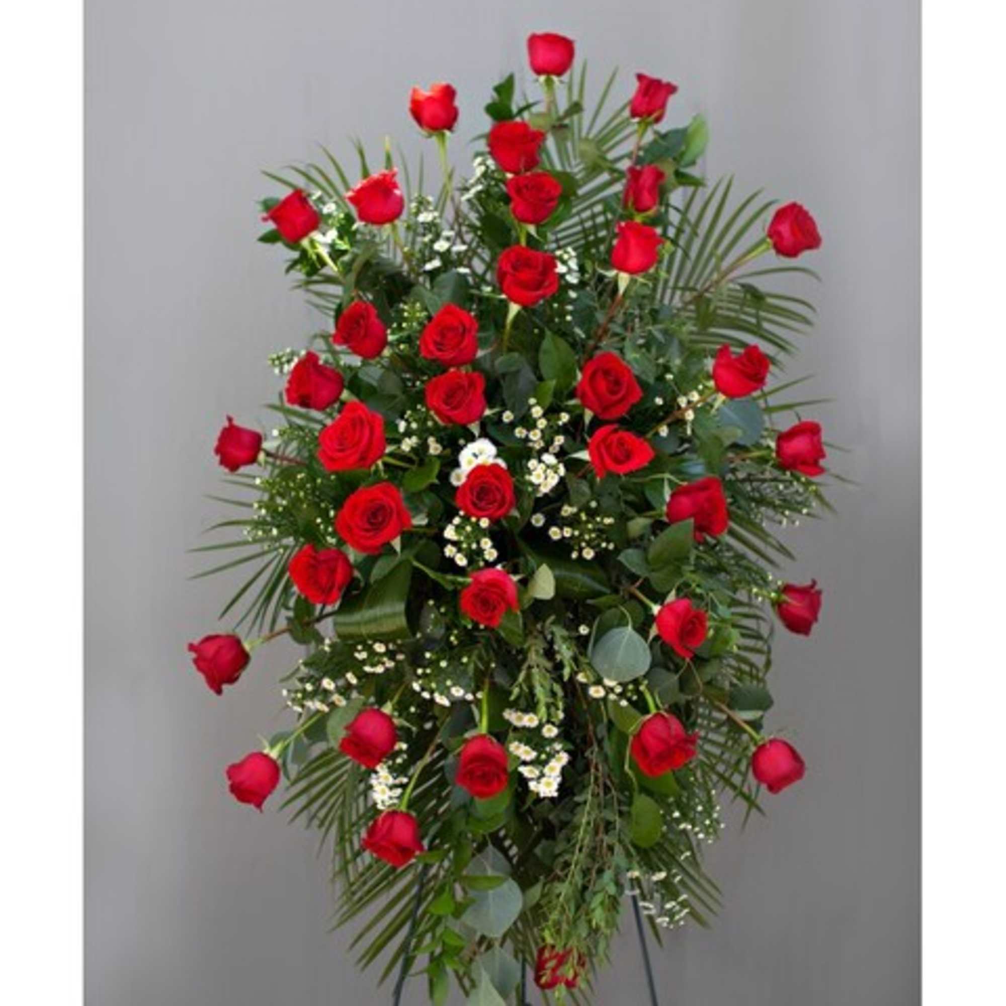 Standing spray of red roses with greenery on a metal easel