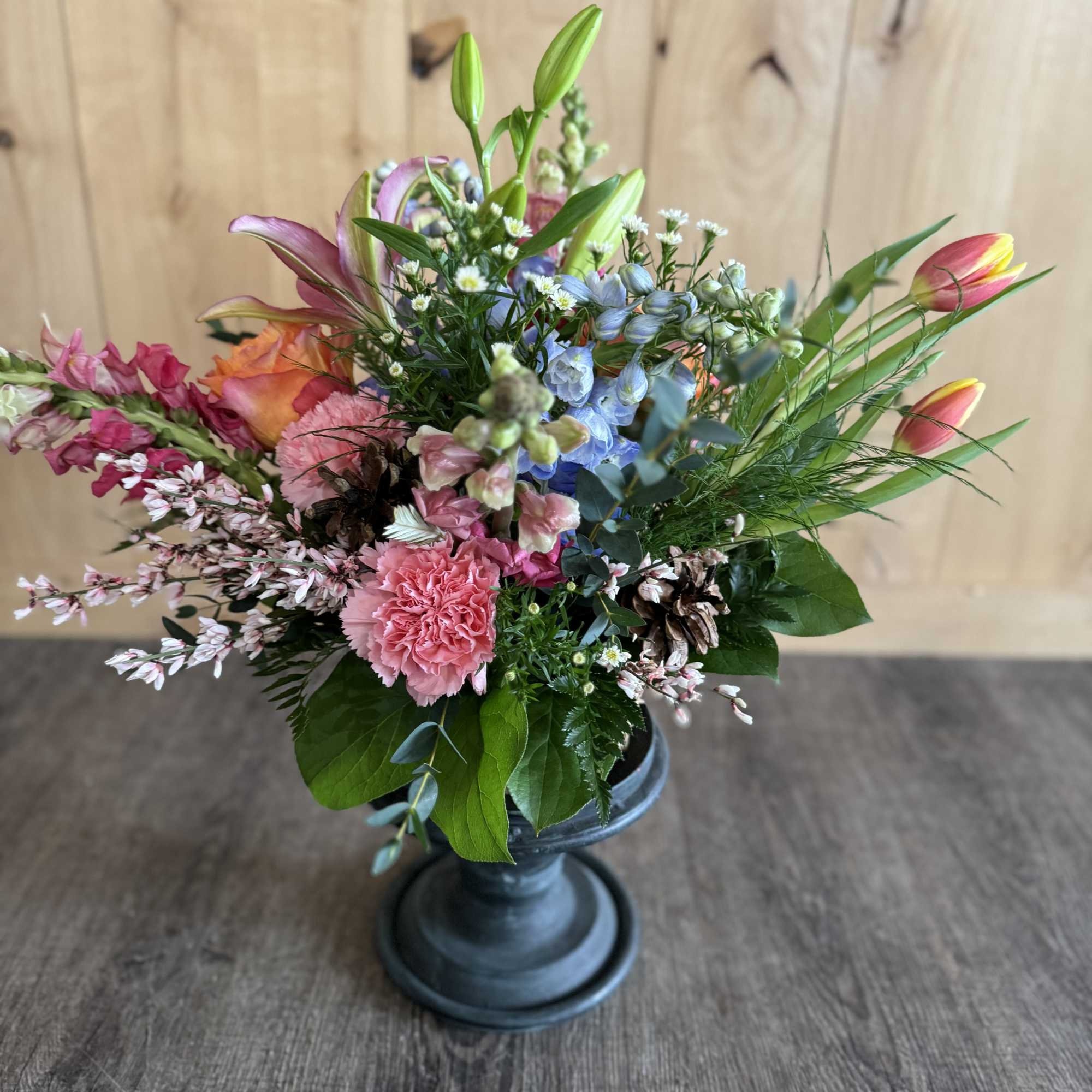 Mixed bouquet in a dark pedestal vase with pink, blue, and orange blooms