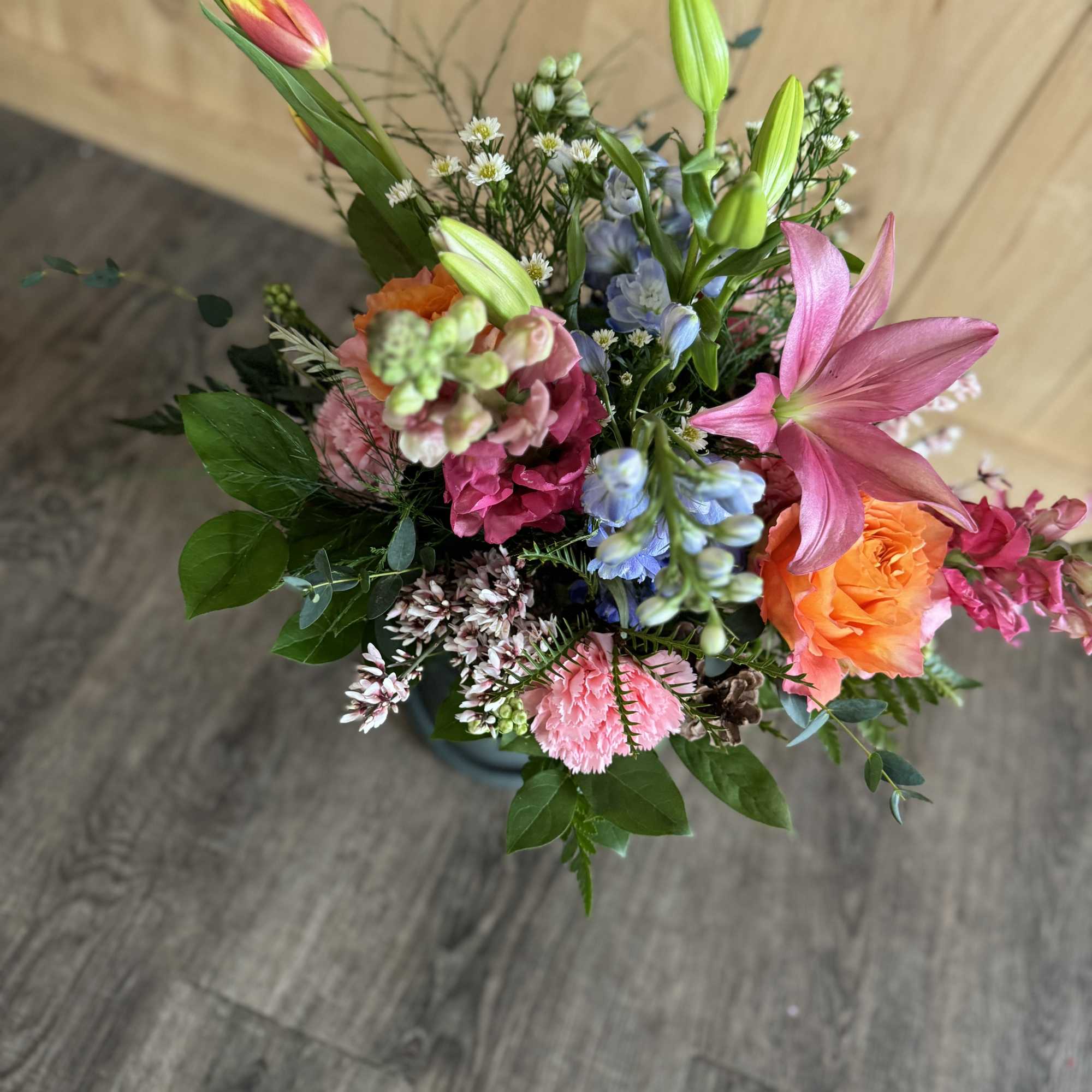 Mixed bouquet with pink lilies, orange roses, and blue flowers in a vase