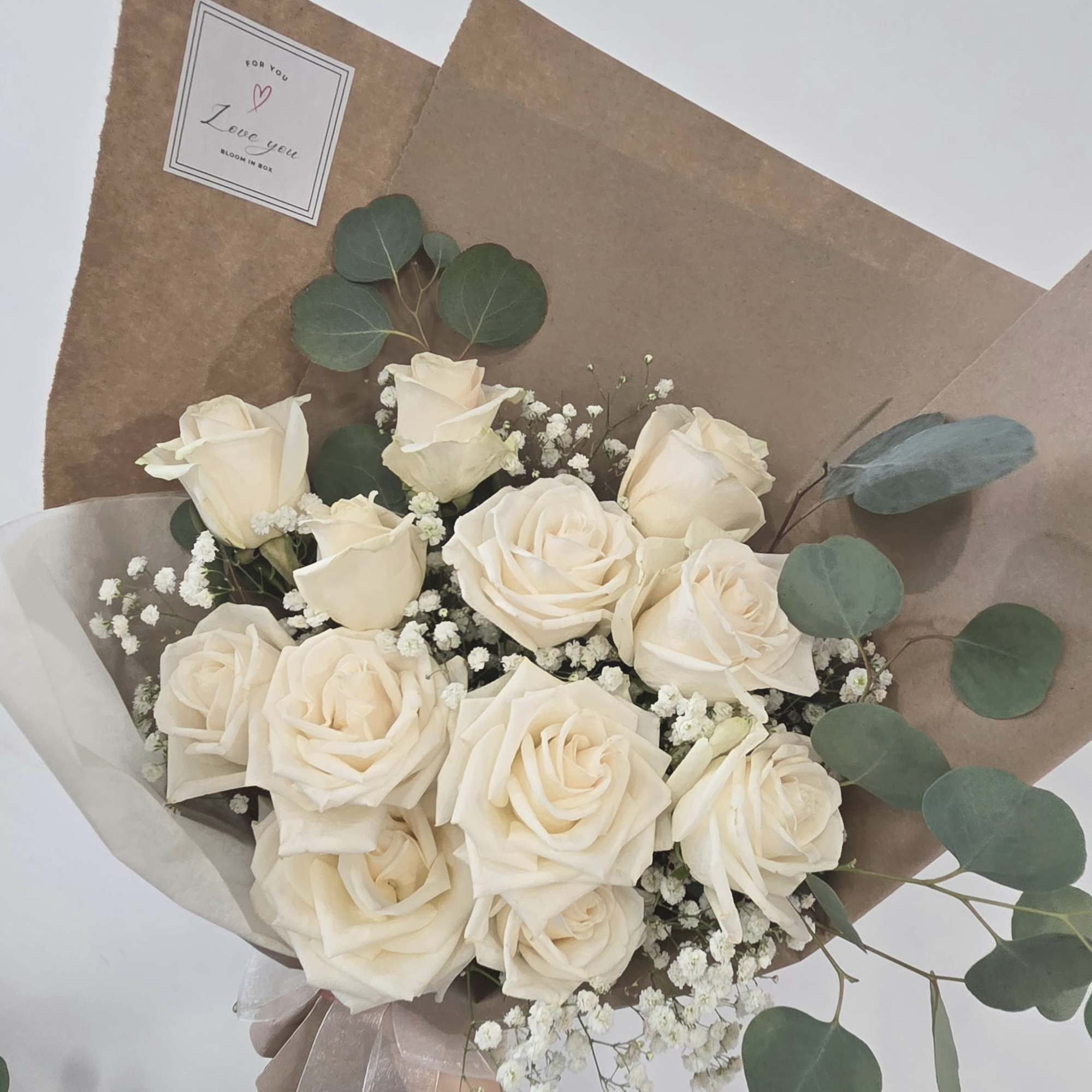 Bouquet of cream roses with baby's breath and eucalyptus in brown paper