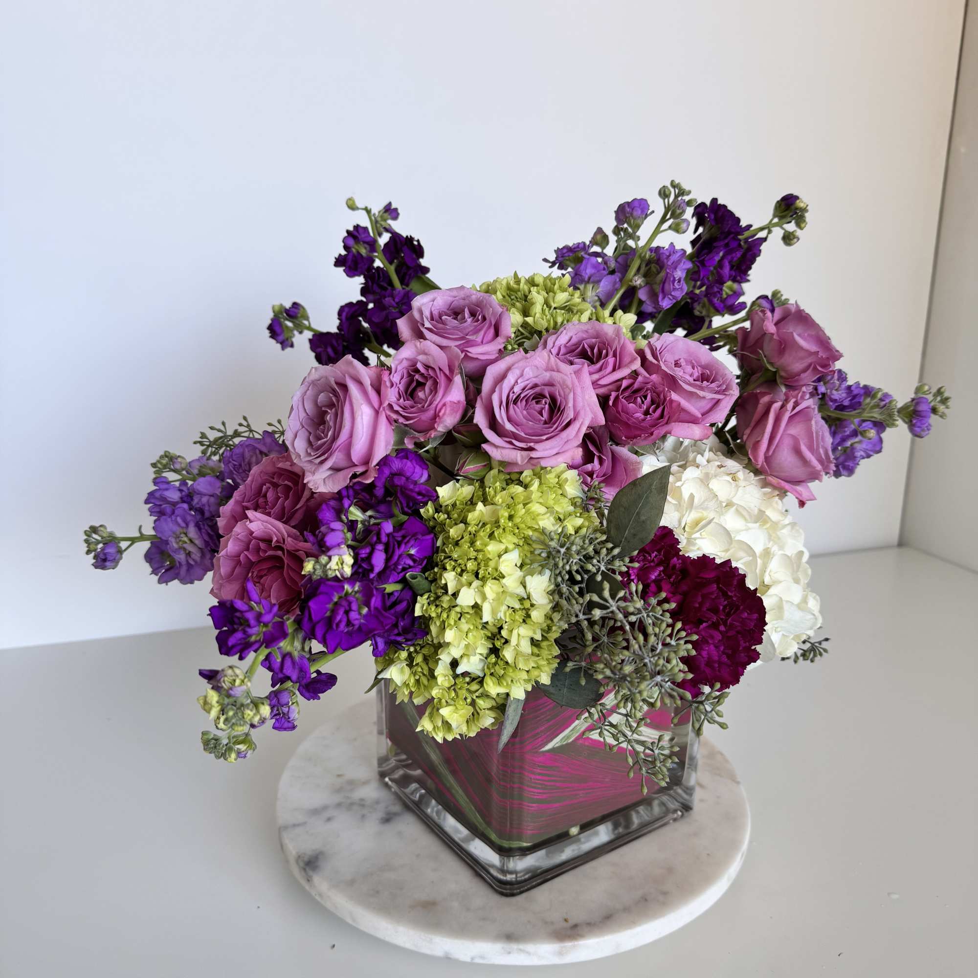 A lush cluster of blush and lavender roses paired with vivid purple