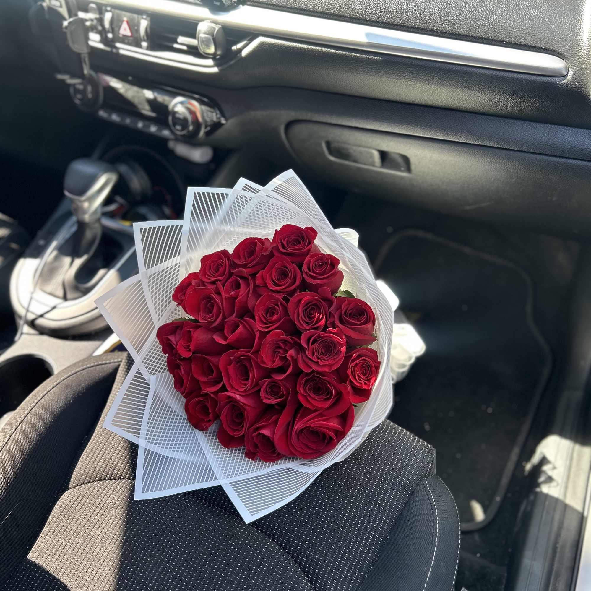 Bouquet of red roses wrapped in white paper on a car seat