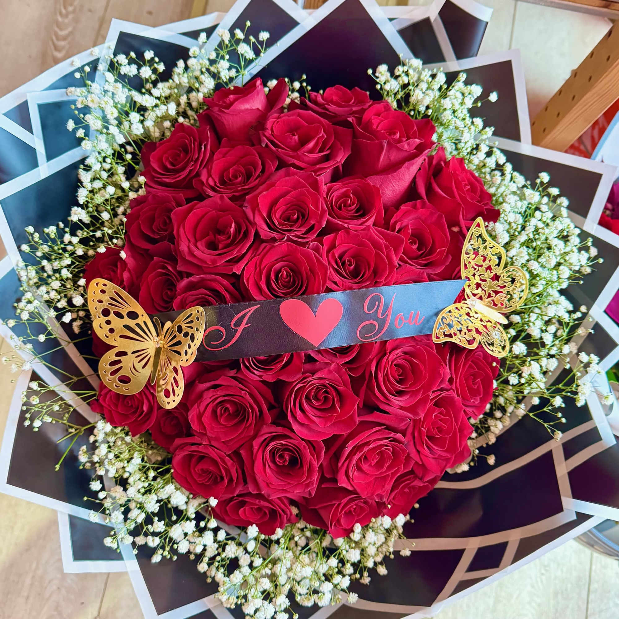 Heart-shaped bouquet of red roses with white baby's breath and a "I ♥ You" ribbon