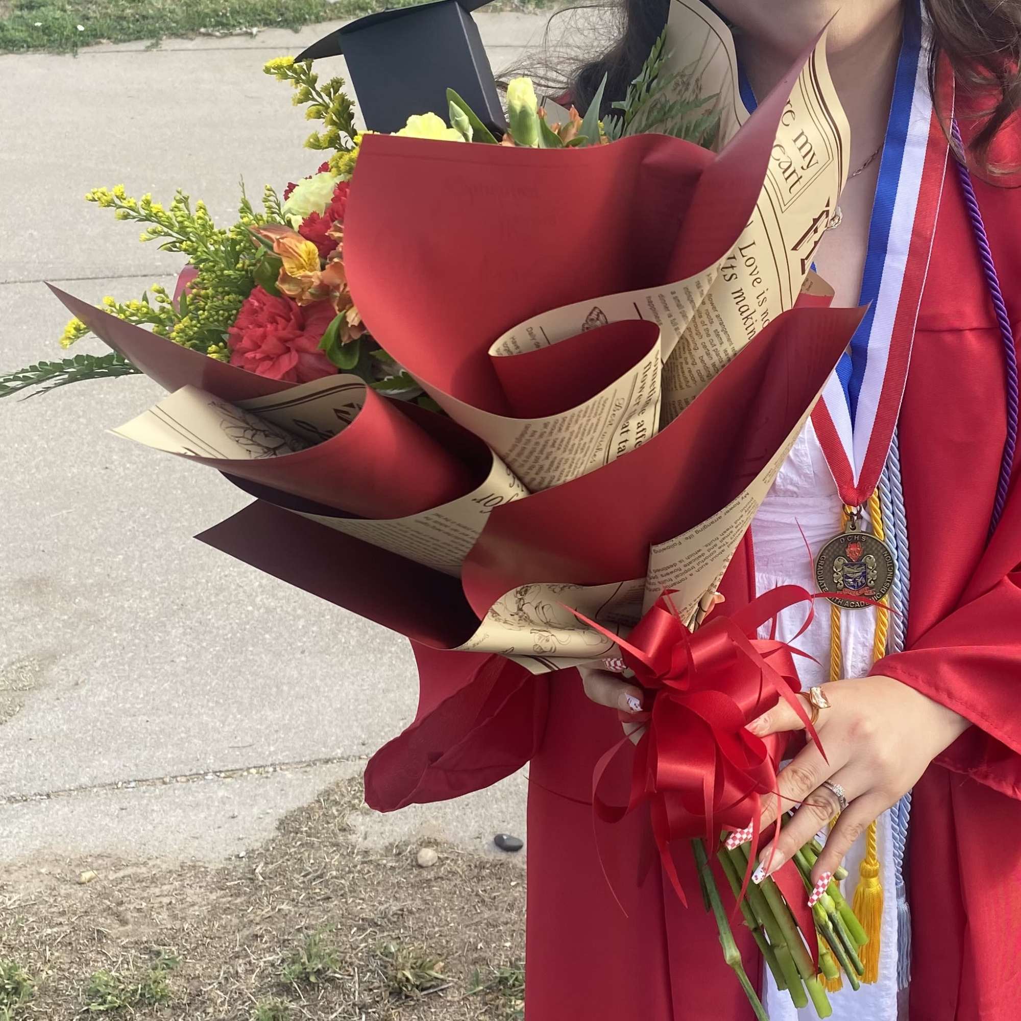 Graduate holding a wrapped bouquet of mixed flowers with a red ribbon