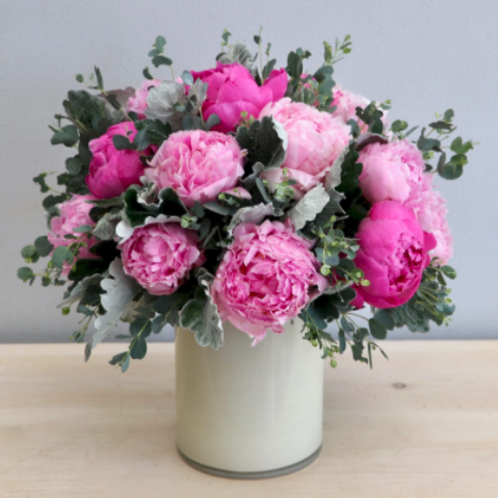 Round arrangement of pink peonies in a white cylinder vase