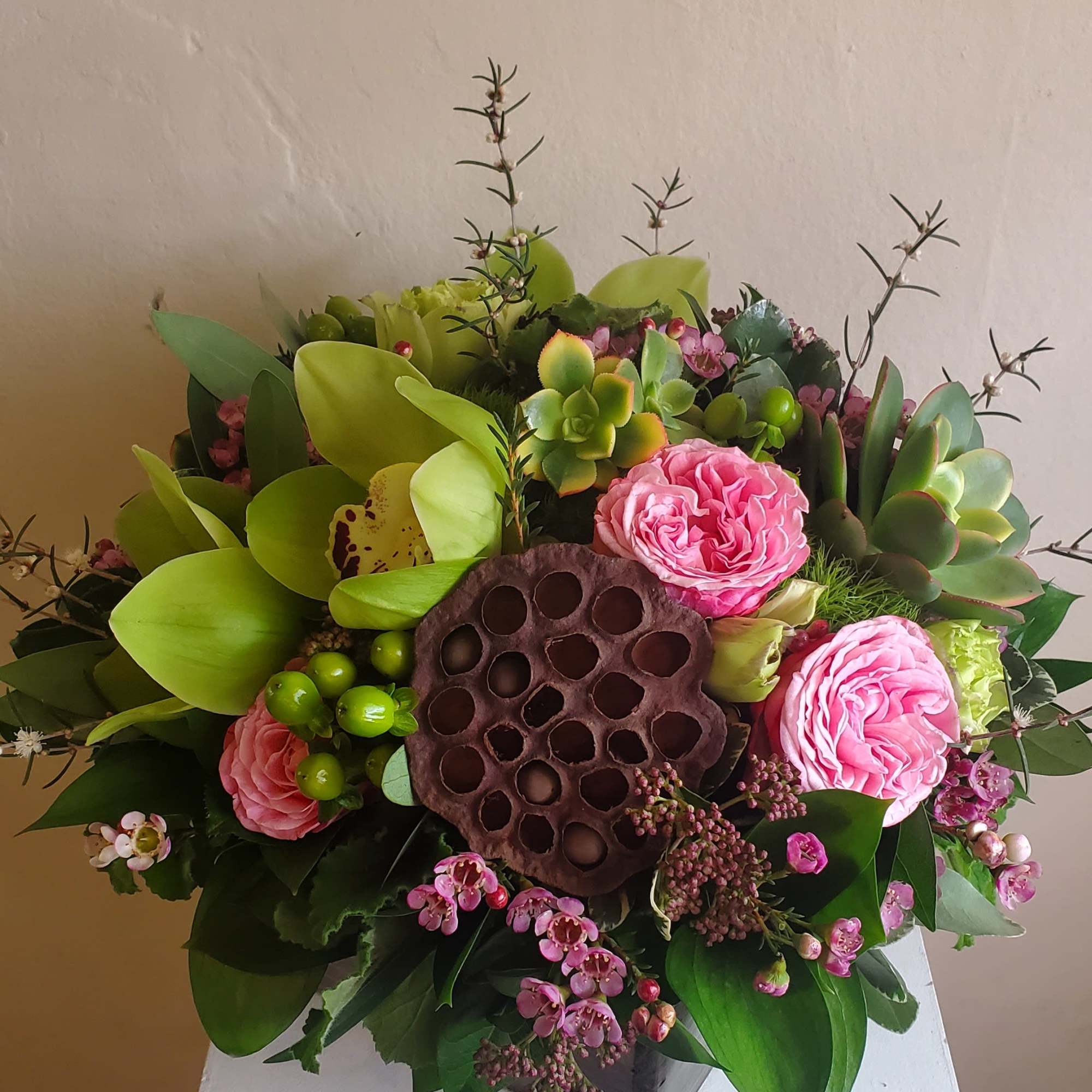 Pink roses and succulents arranged around a lotus seed pod in a square vase