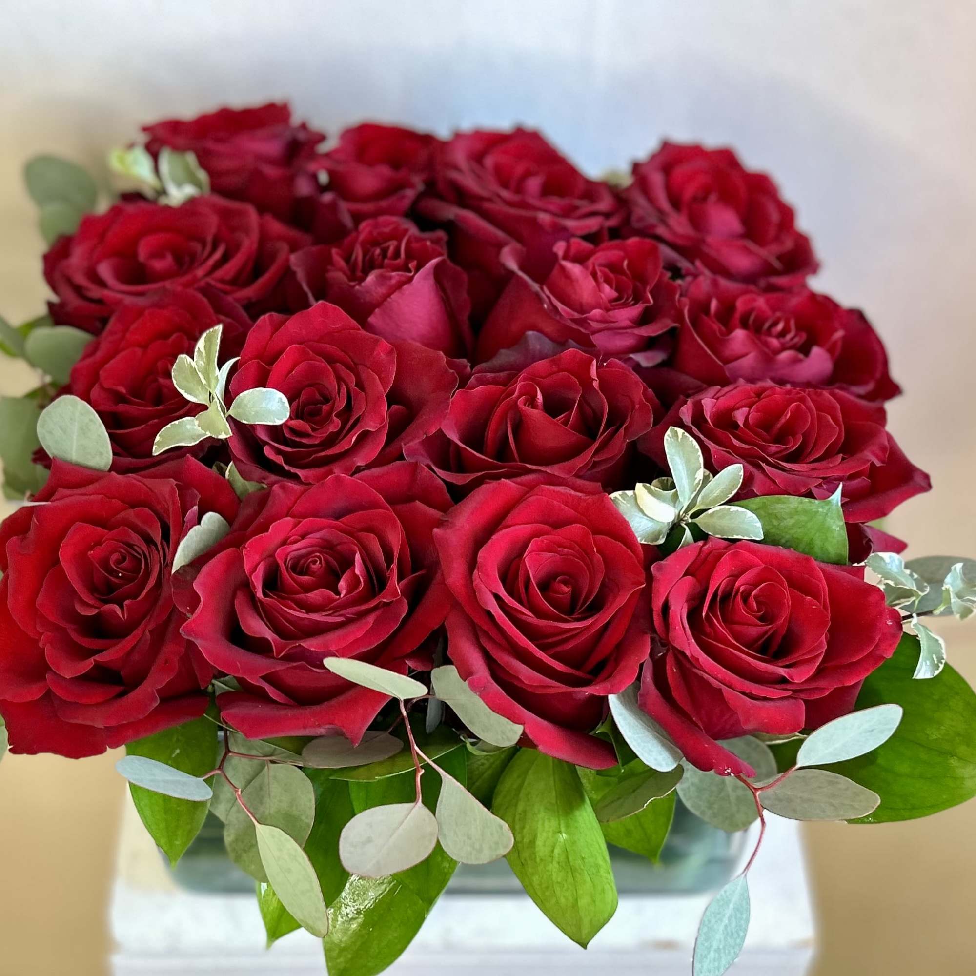 A bouquet of red roses with eucalyptus in a clear vase
