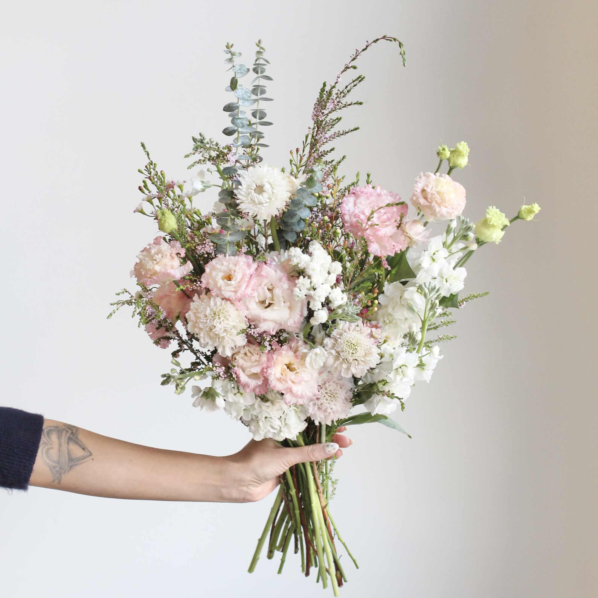 Handheld bouquet of pink and white flowers with tall eucalyptus stems