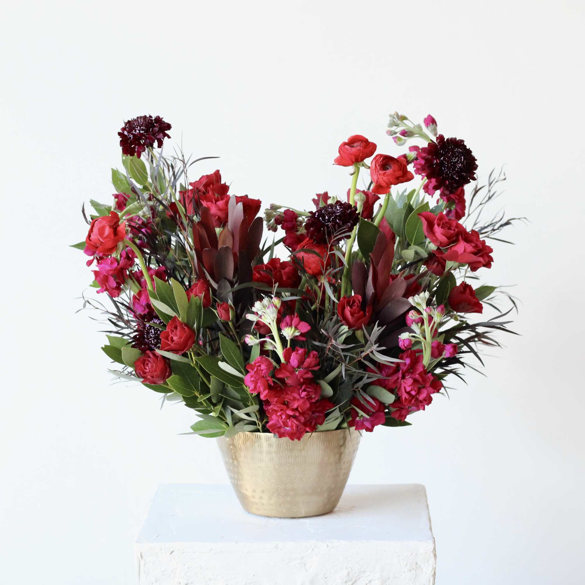 Red and pink floral arrangement in a gold vase