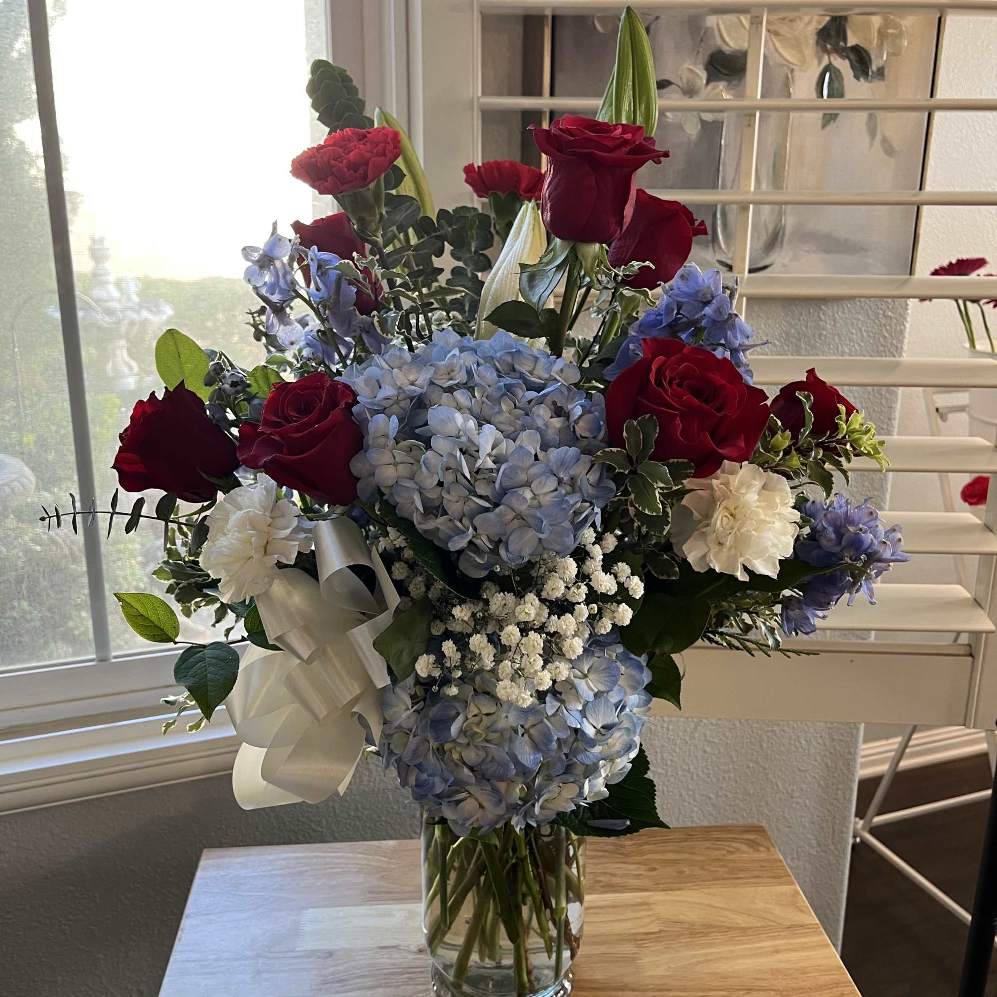 Mixed bouquet of red roses, blue hydrangeas, and white flowers in a glass vase